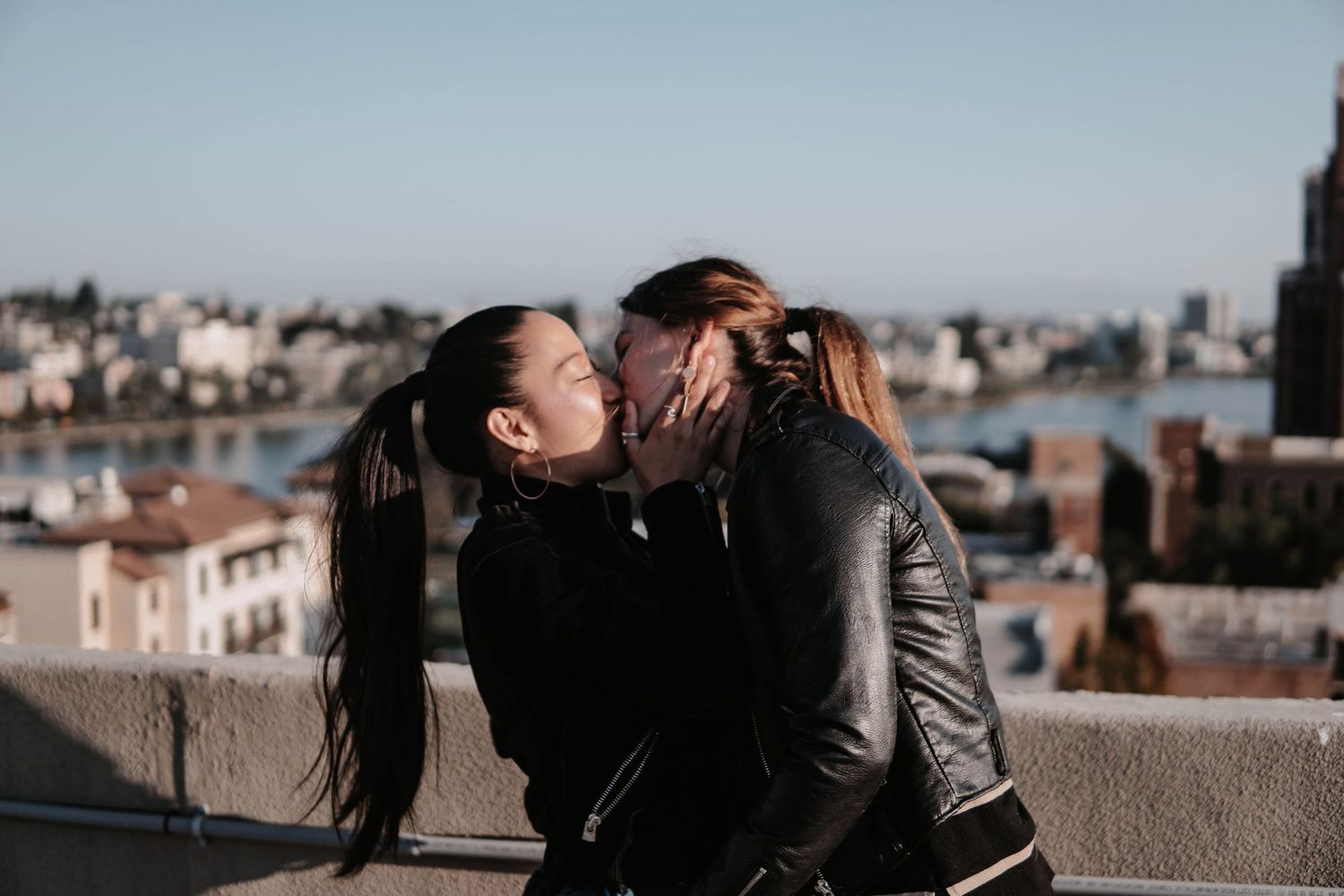 Joyful couple embracing and smiling on a rooftop with a bright city skyline and water views in the background at golden hour