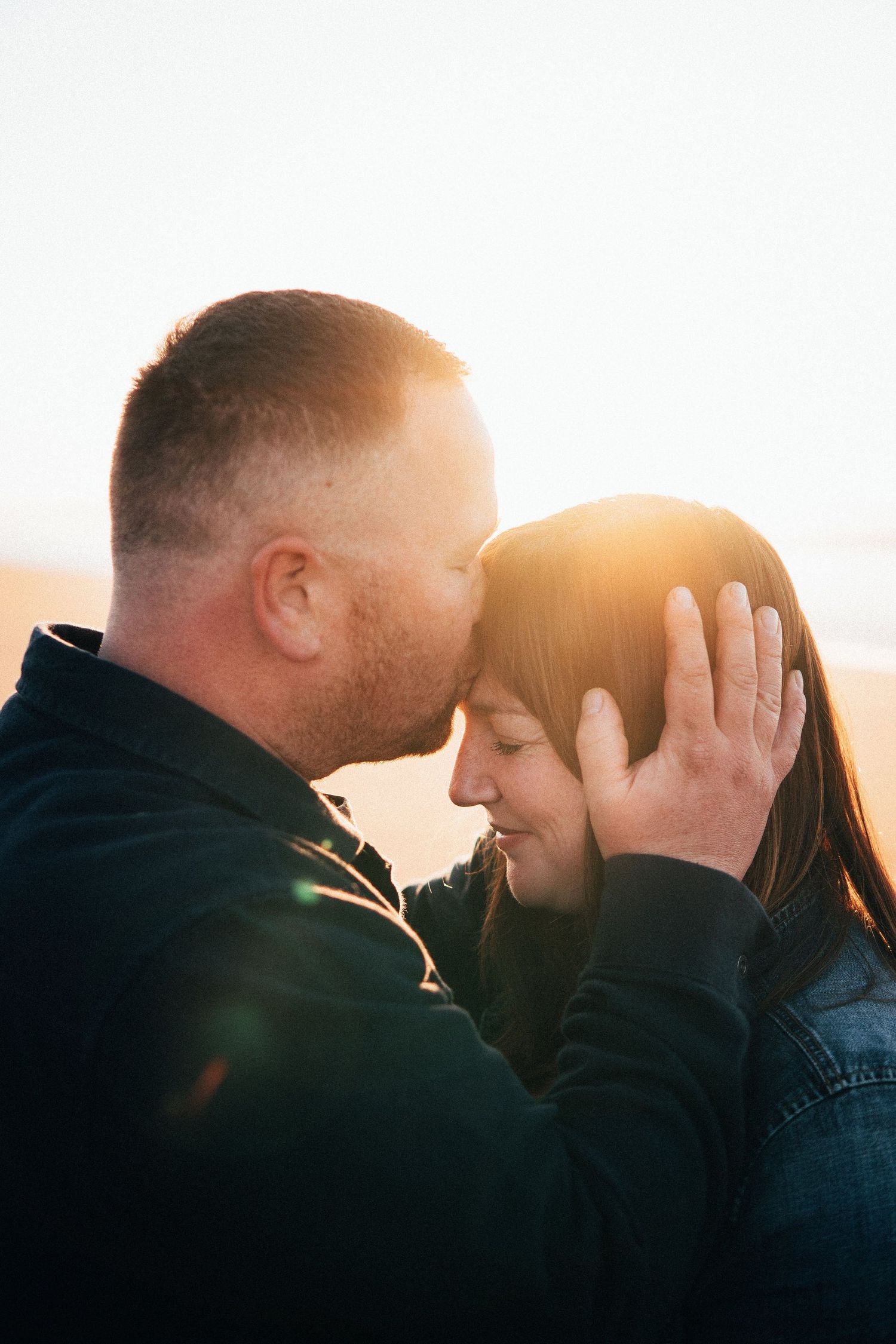 Couple embracing on the beach at sunset with soft golden light, captured in a tender moment that highlights love, warmth, and passion.