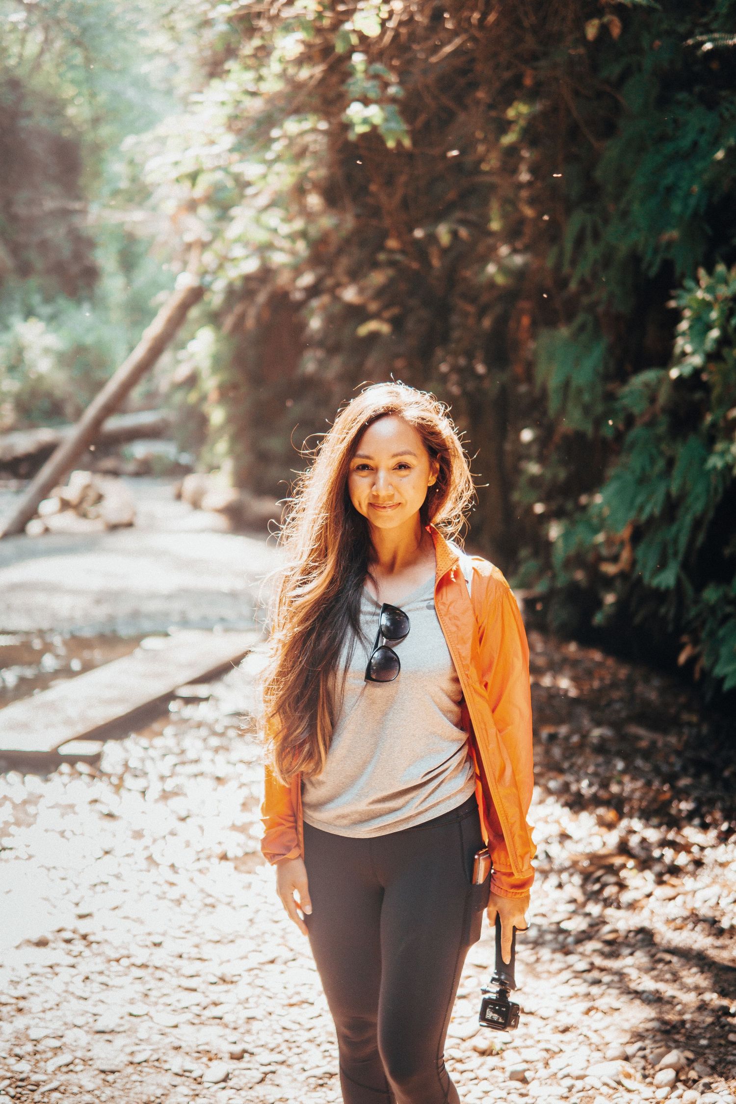 Bright outdoor adventure portrait of a woman hiking through a sunlit forest trail, highlighting minimal, natural, and travel-inspired vibes.