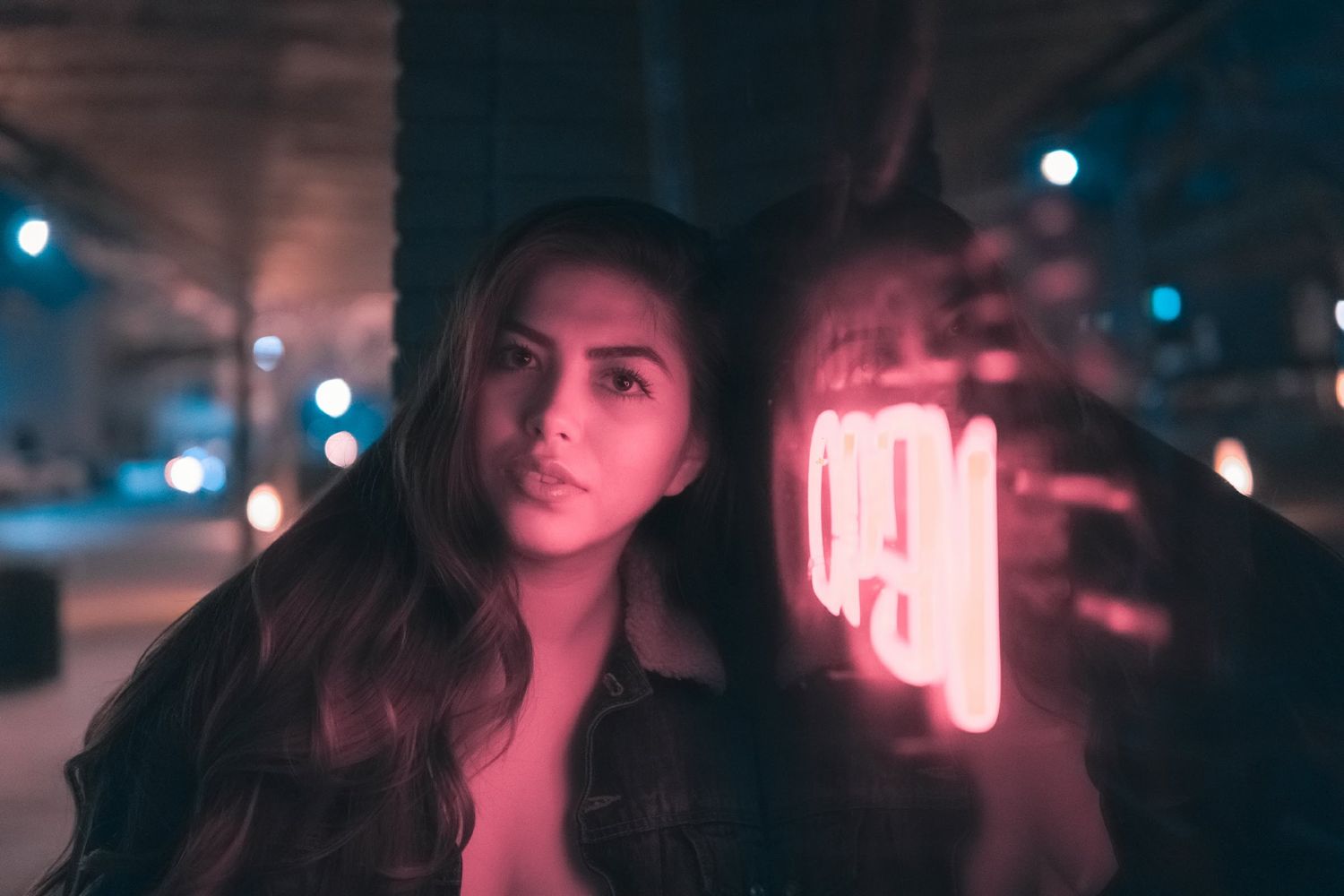 Night portrait of a woman beside a glowing pink neon OPEN sign, moody urban lighting and reflections creating a dreamy cinematic feel.