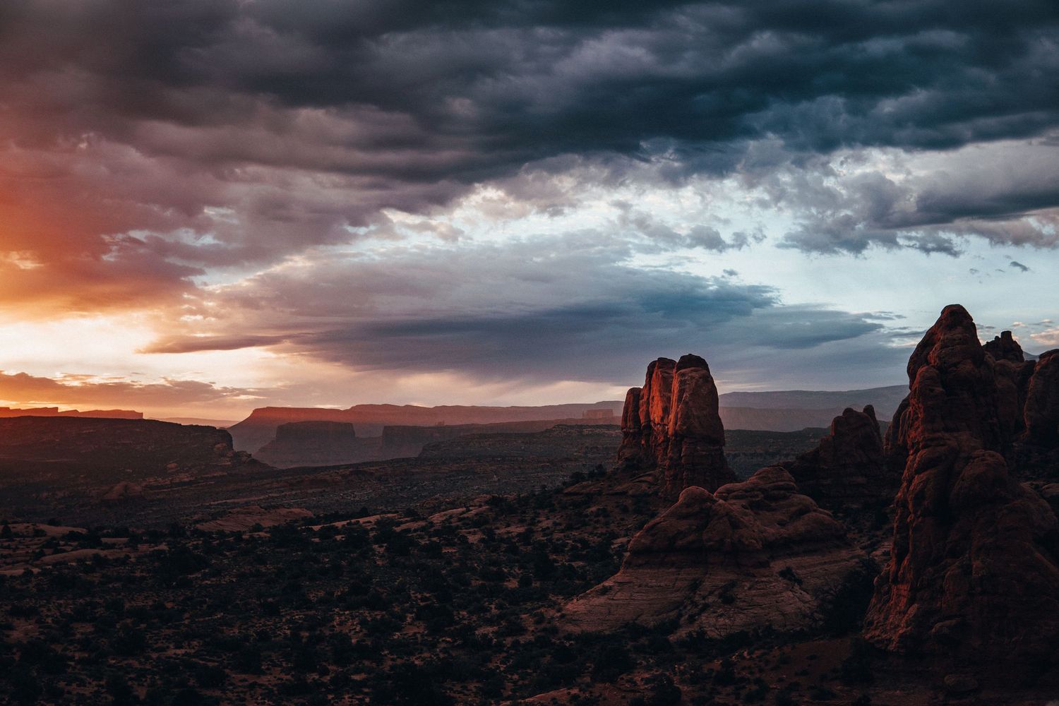 Moody desert landscape at sunset with red rock formations glowing under dramatic storm clouds, capturing a rugged, adventure-filled scene.