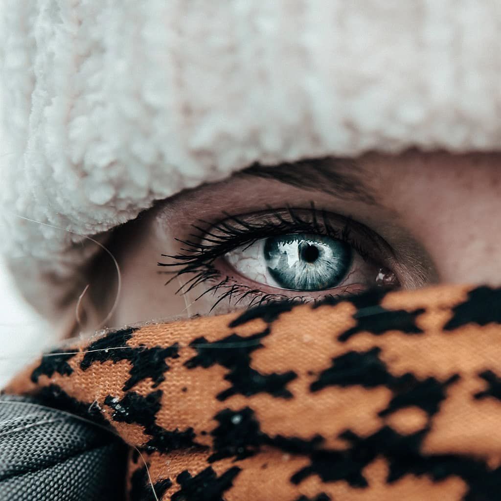 Winter adventure close-up of bright blue eyes wrapped in cozy gear, emphasizing minimal detail, natural light, and outdoor exploration vibes