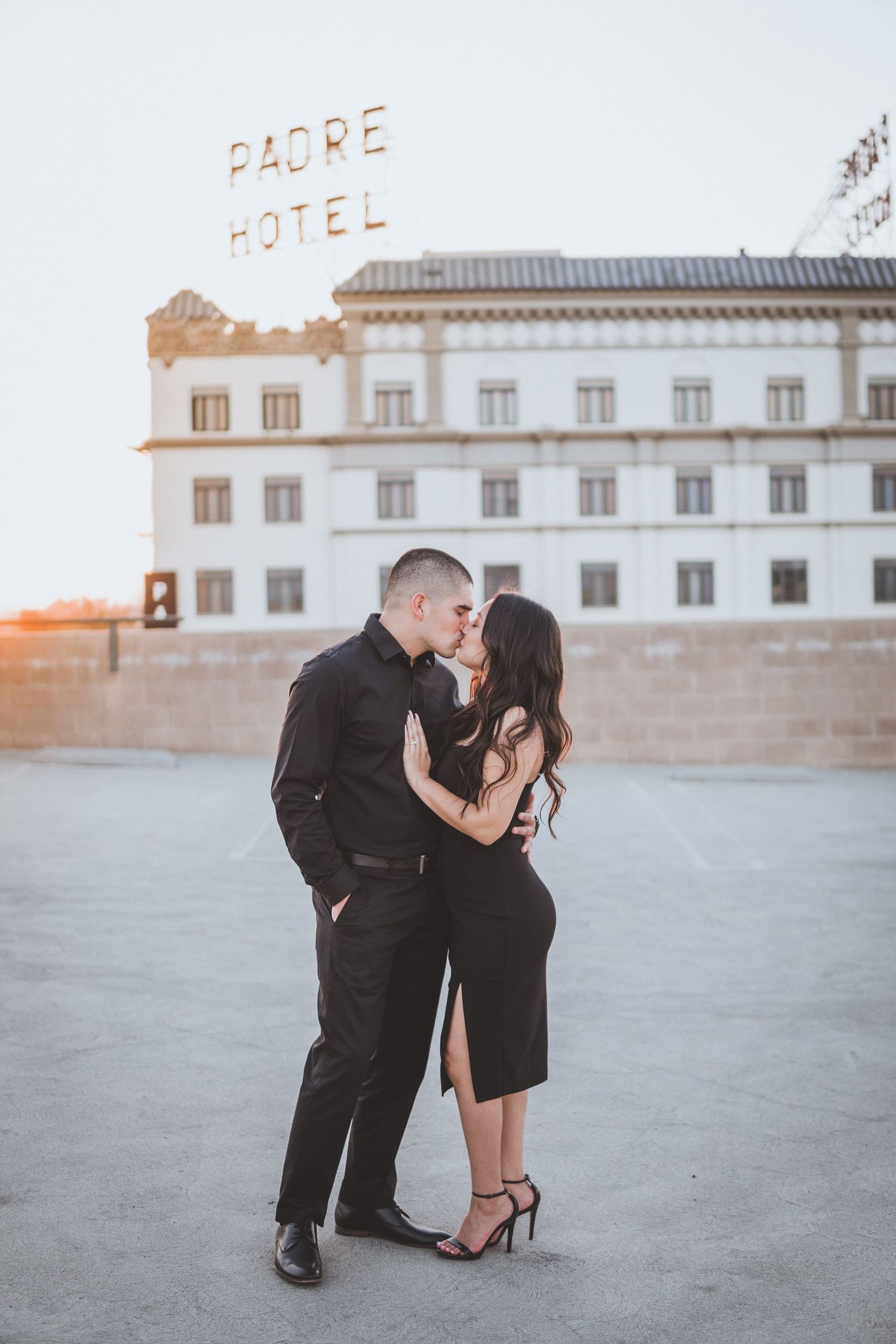 Elegant couple embracing on a rooftop at sunset with a historic hotel sign in the background, creating a romantic urban portrait scene