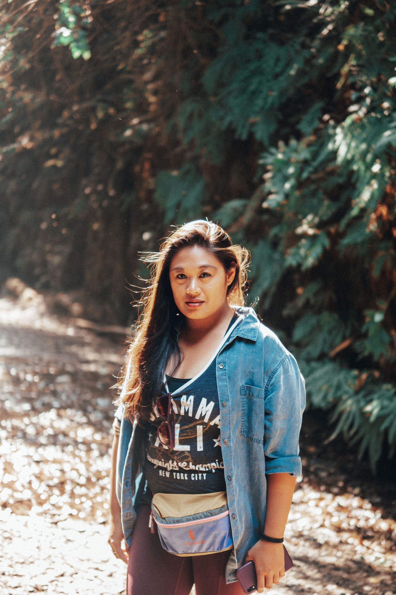 Minimal adventure portrait of a woman on a forest trail in soft sunlight, blending natural tones, outdoor exploration, and modern lifestyle.