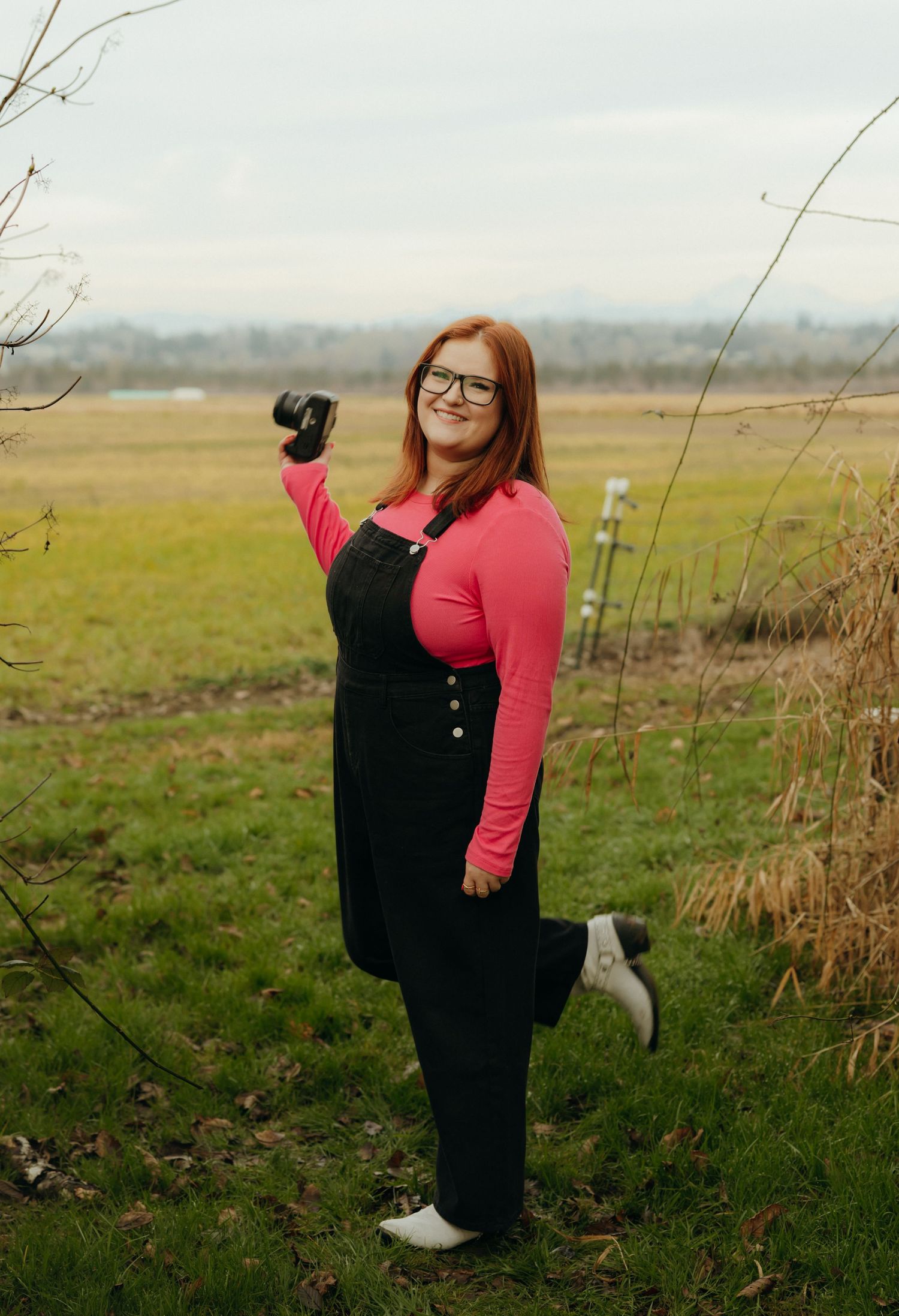 A person in a black and coral outfit stands in a grassy field on an overcast day.
