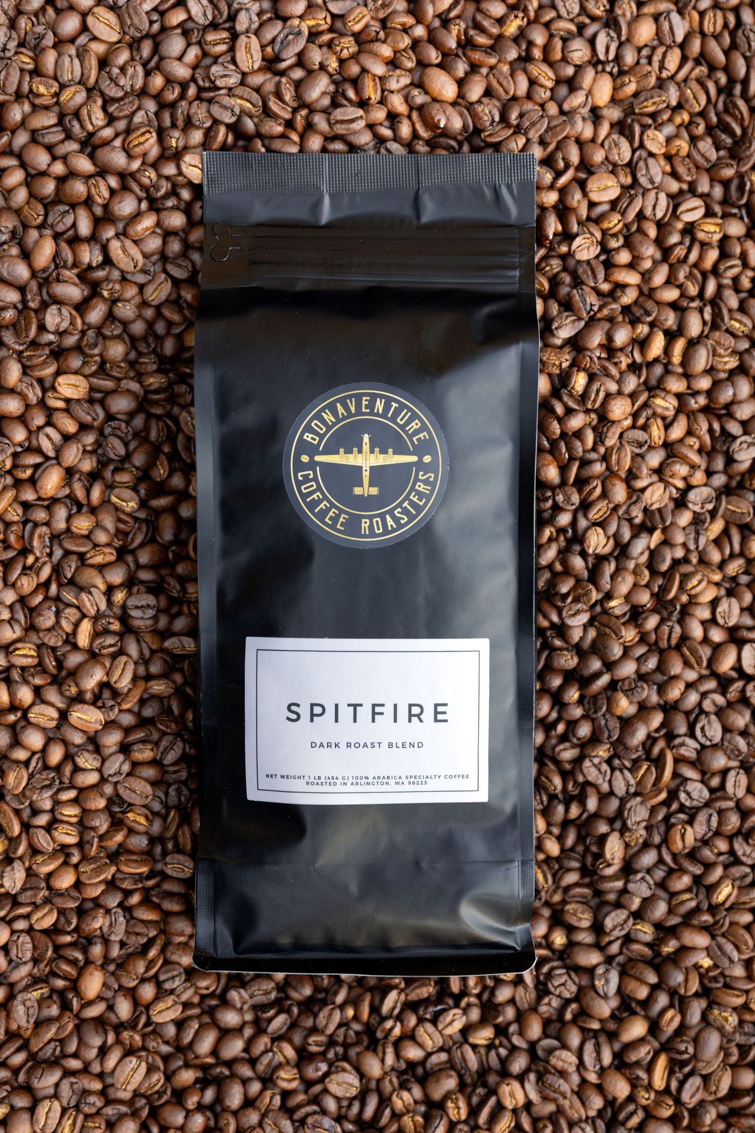Bonaventure Coffee Roasters Spitfire Dark Roast Blend in black bag surrounded by roasted coffee beans.