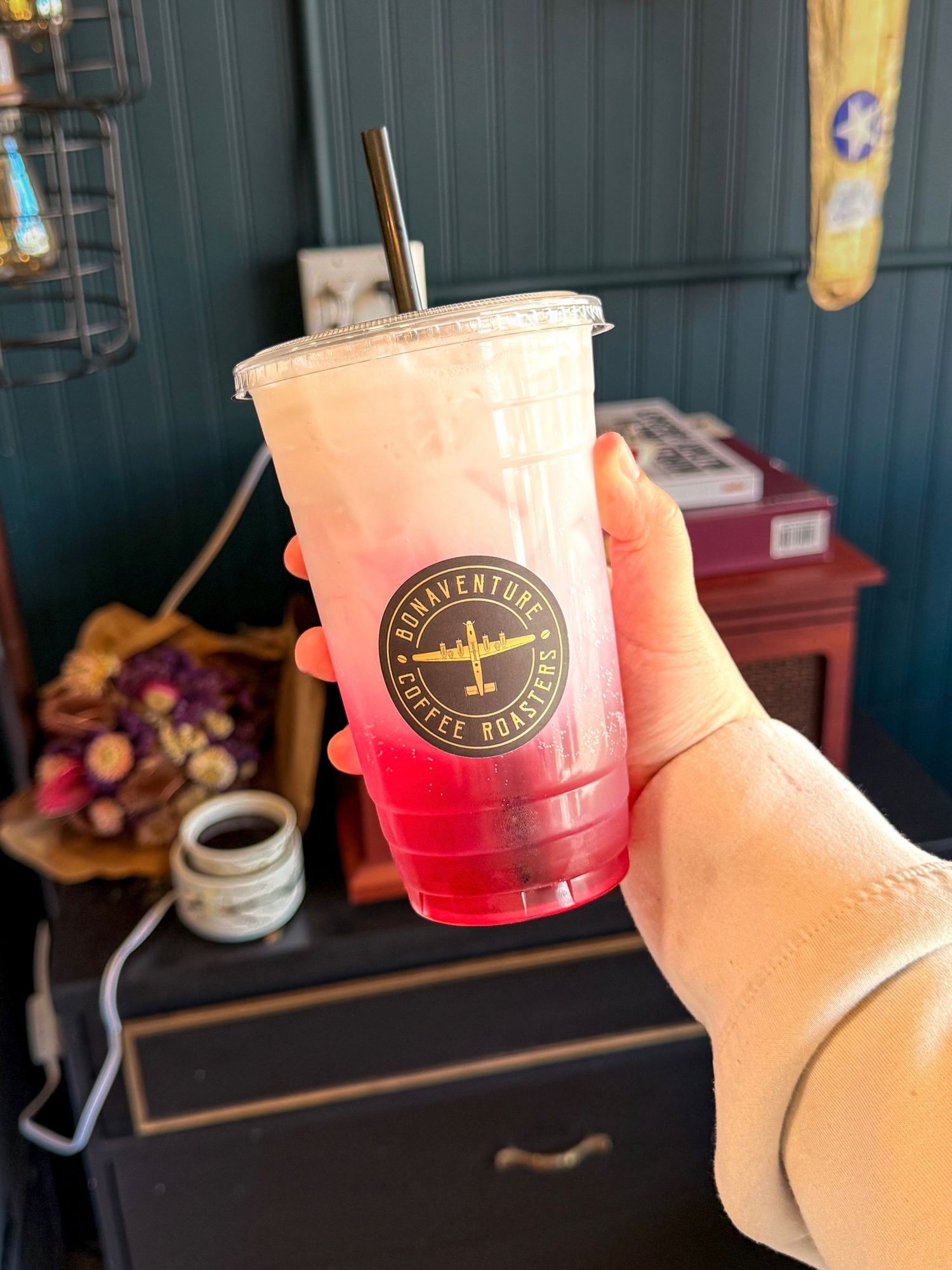 Hand holding a pink iced drink from Bonaventure Coffee Roasters in a clear cup with a metal straw.