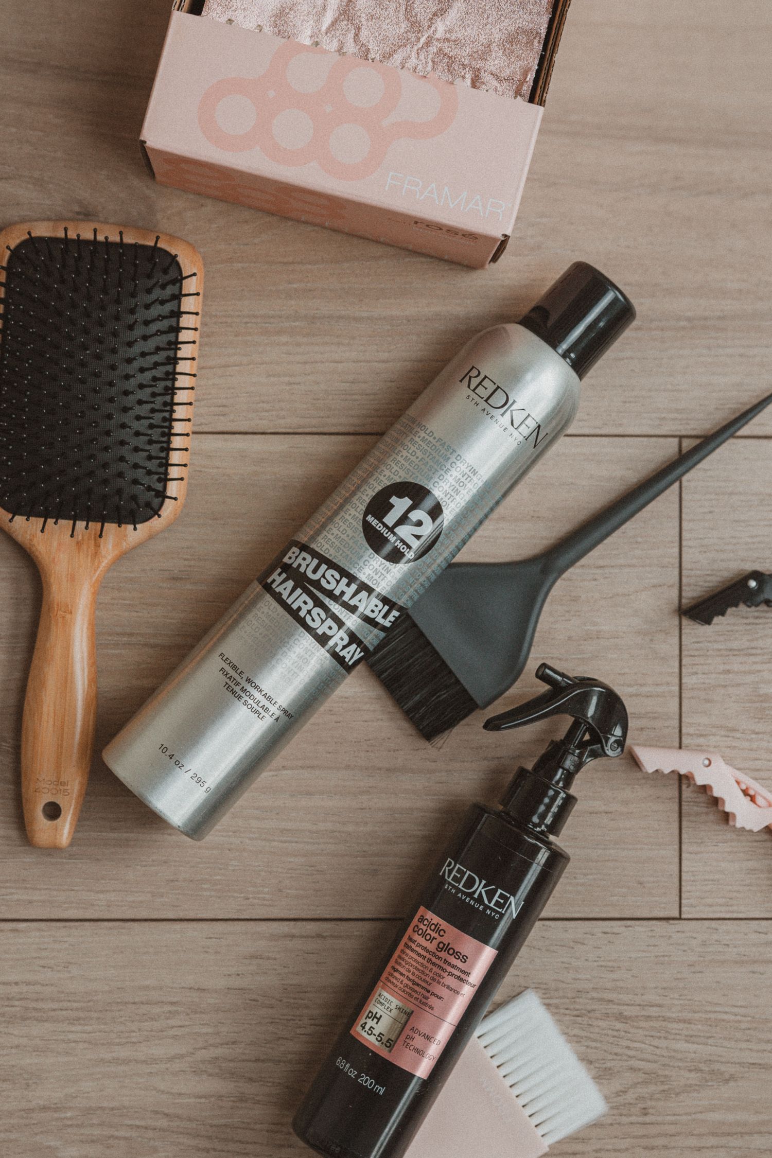 Hair styling products and tools including Redken hairspray, wooden brush, and hair dye application tools on wooden surface.