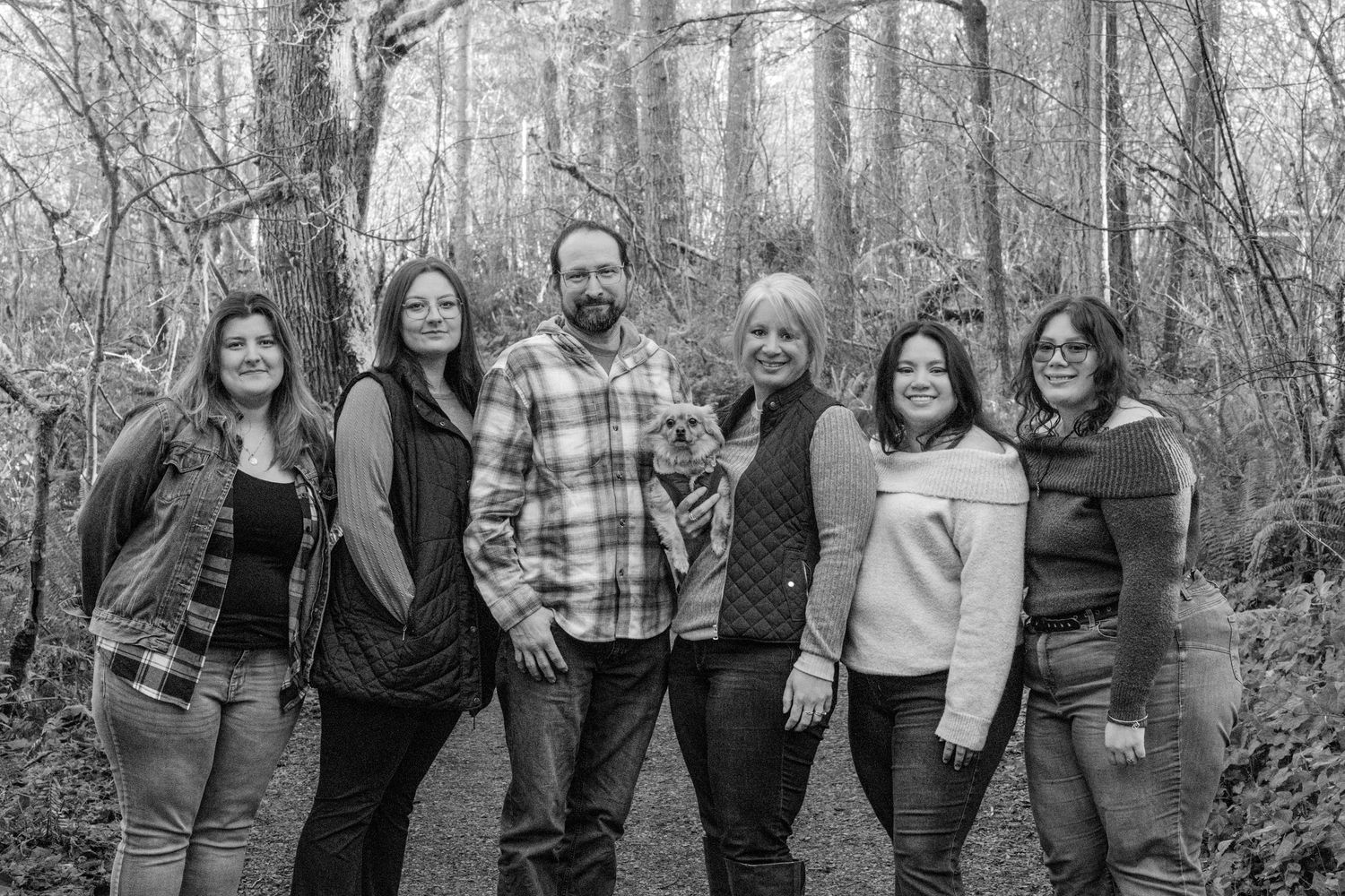 A group of six people stand together smiling on a forest trail in black and white.