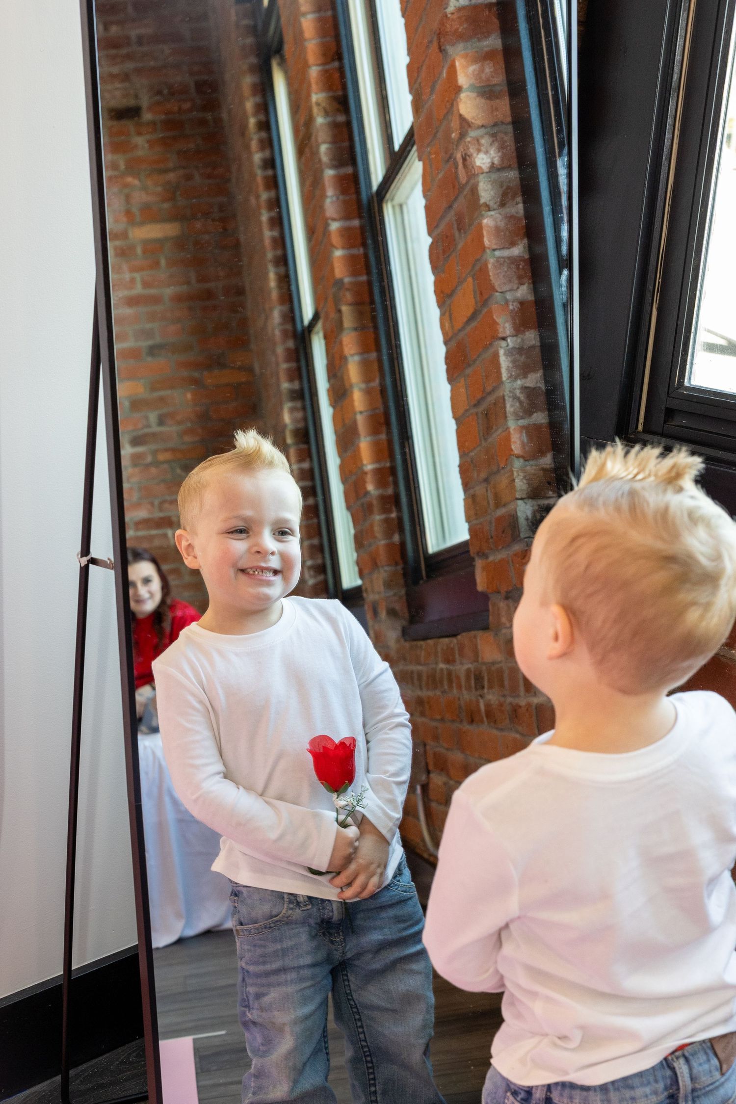 Two children in white shirts play and laugh together in front of exposed brick walls and windows.