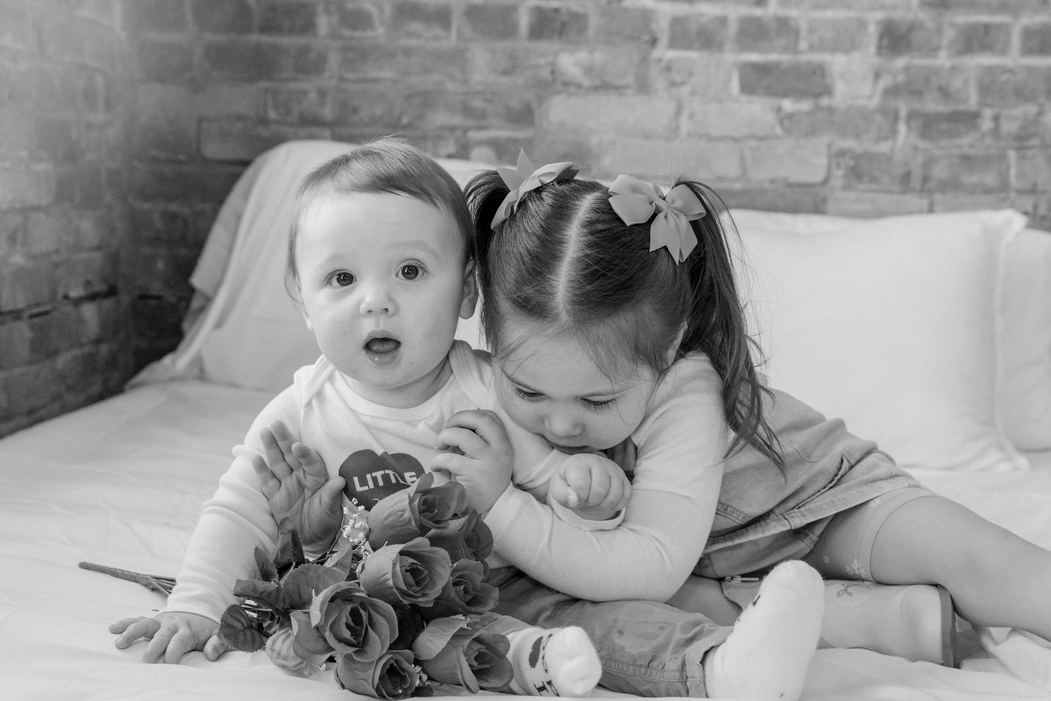 Black and white photo of two young children sitting together on a couch with flowers.