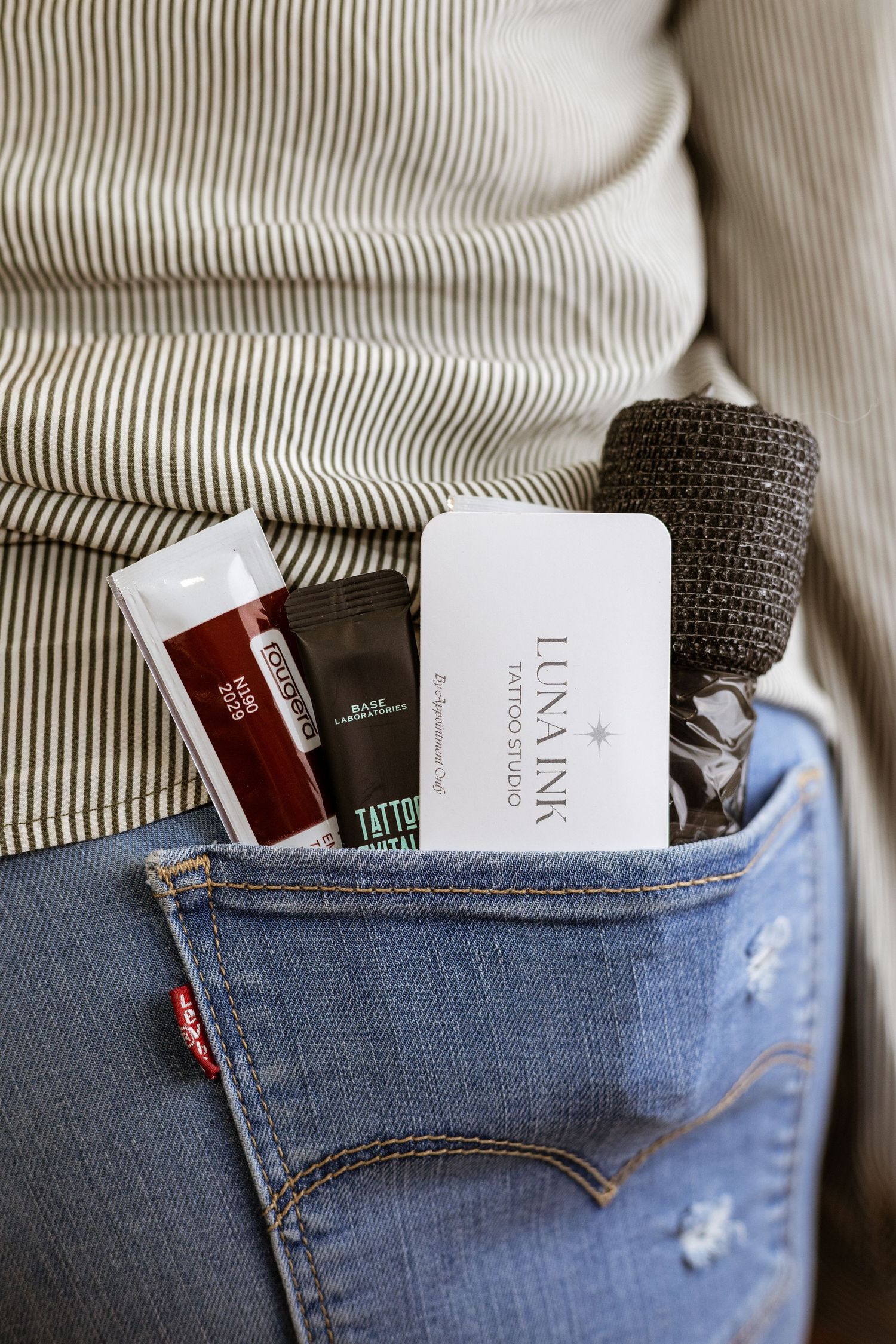 Product samples and testers peeking out of a denim jeans pocket against a white striped fabric background.