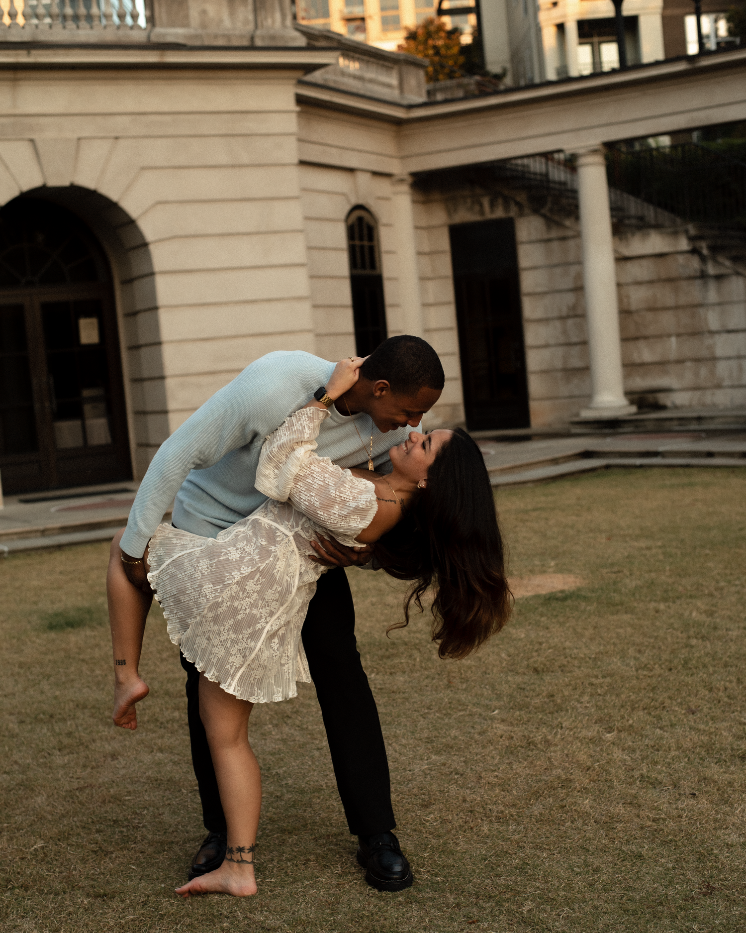 A couple performs a romantic dance dip pose on a grassy lawn in front of a grand stone building.