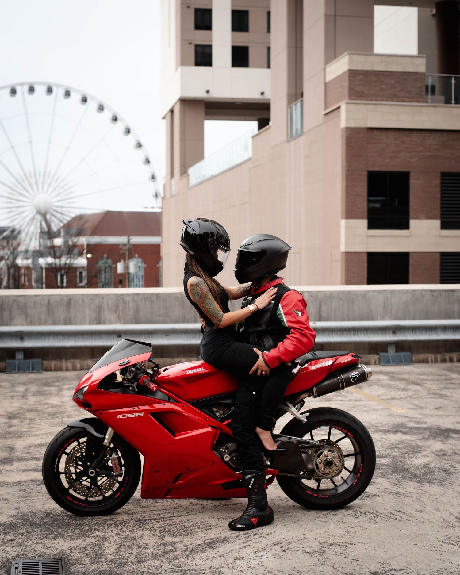 A red Ducati motorcycle parked in front of a building with a ferris wheel visible in the background.