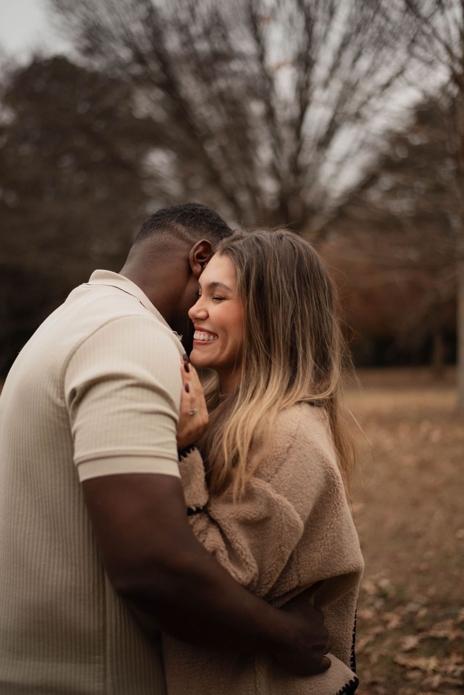 Intimate autumn couple photoshoot showing tender embrace against backdrop of bare trees in warm earth tones.