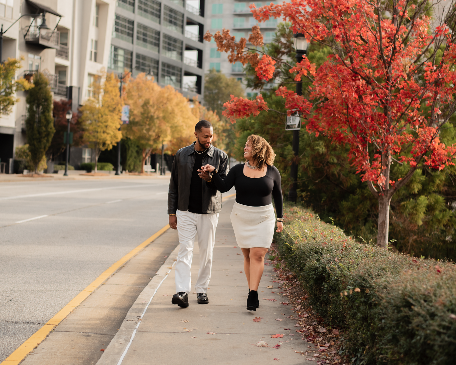 A person walking on a sidewalk past vibrant red autumn trees and residential buildings.