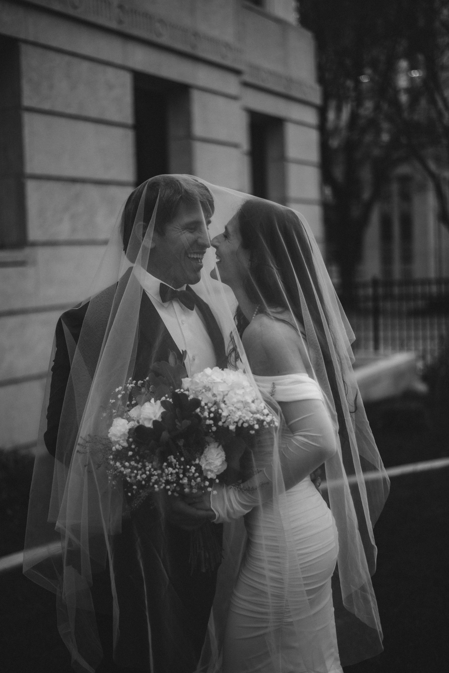 A black and white wedding photo series showing tender moments between a bride and groom in front of a building.