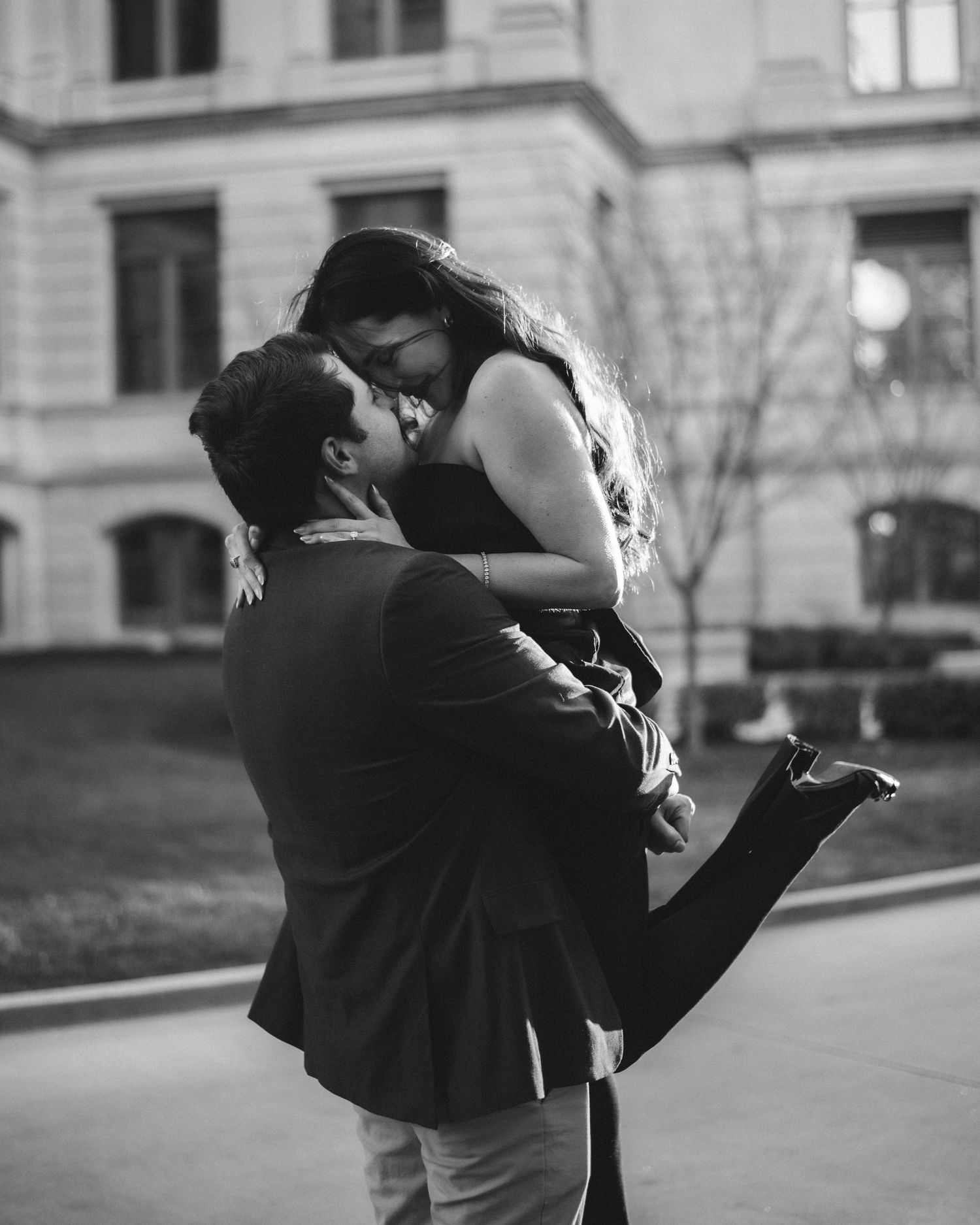 A romantic black and white photograph of a couple embracing on a city street, with one person lifted off the ground.