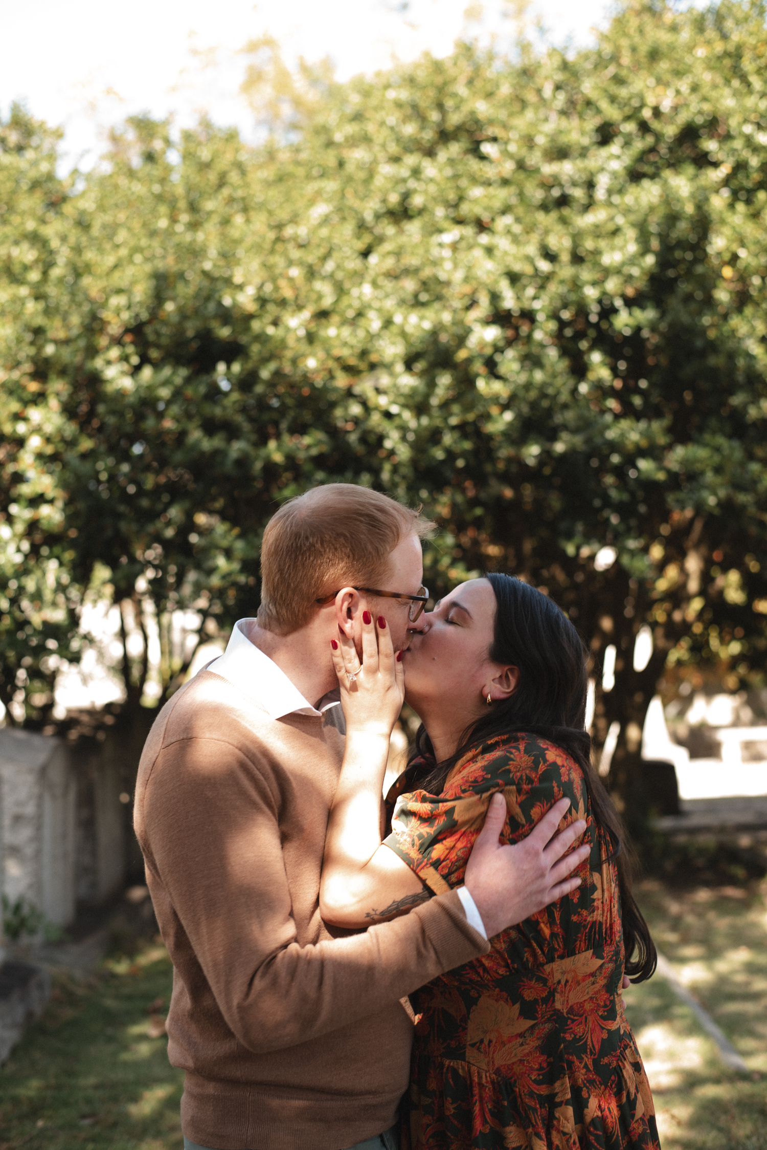 A couple shares a tender moment in an outdoor setting with orange trees in the background during golden hour.