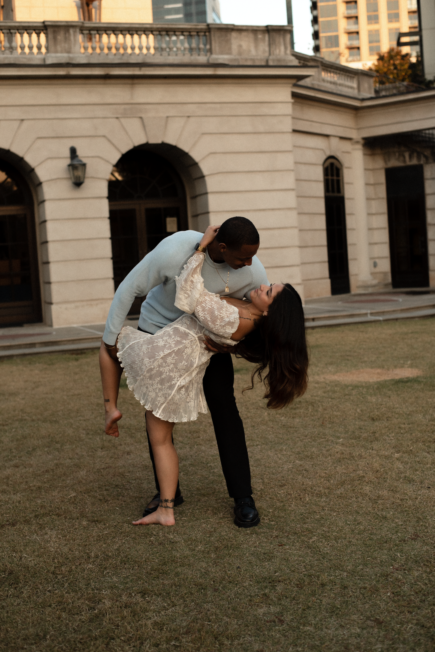 Couple performs romantic dance dips on a manicured lawn with classic architecture in background.