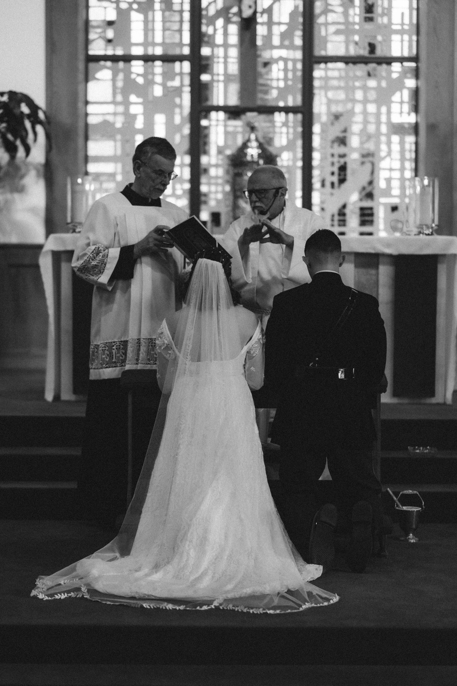 A black and white photograph of a wedding ceremony taking place inside a church with clergy officiating at the altar.