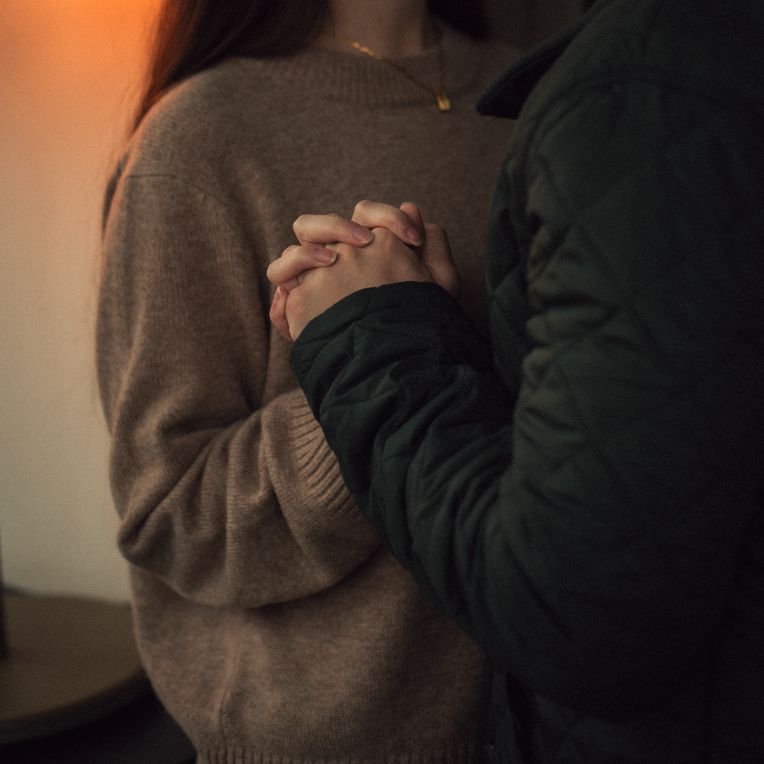 Close up of two people holding hands wearing cozy sweaters in warm lighting.