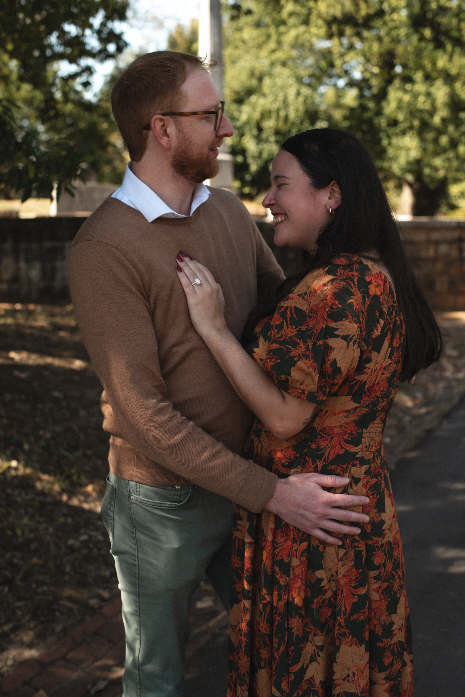 A couple embraces outdoors in autumn, wearing brown and floral clothing while sharing an intimate moment in nature.