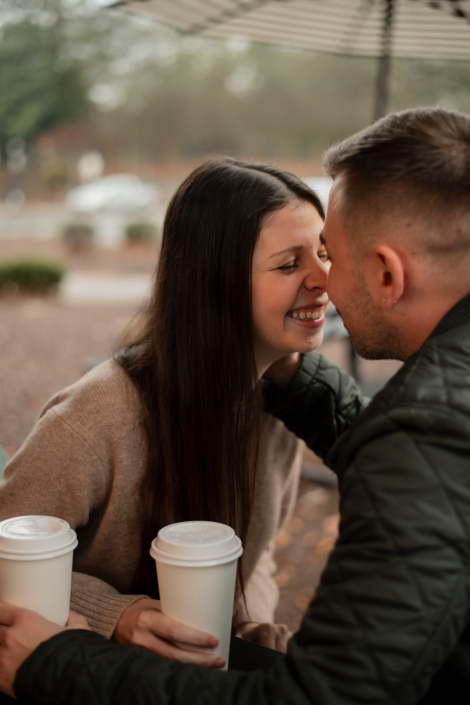 A couple shares intimate moments while holding coffee cups on a cloudy day.