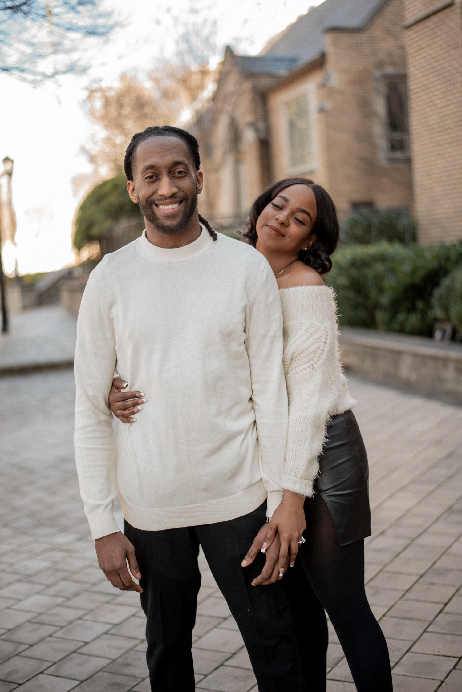 A couple wearing matching cream-colored sweaters share joyful moments together on a stone patio.