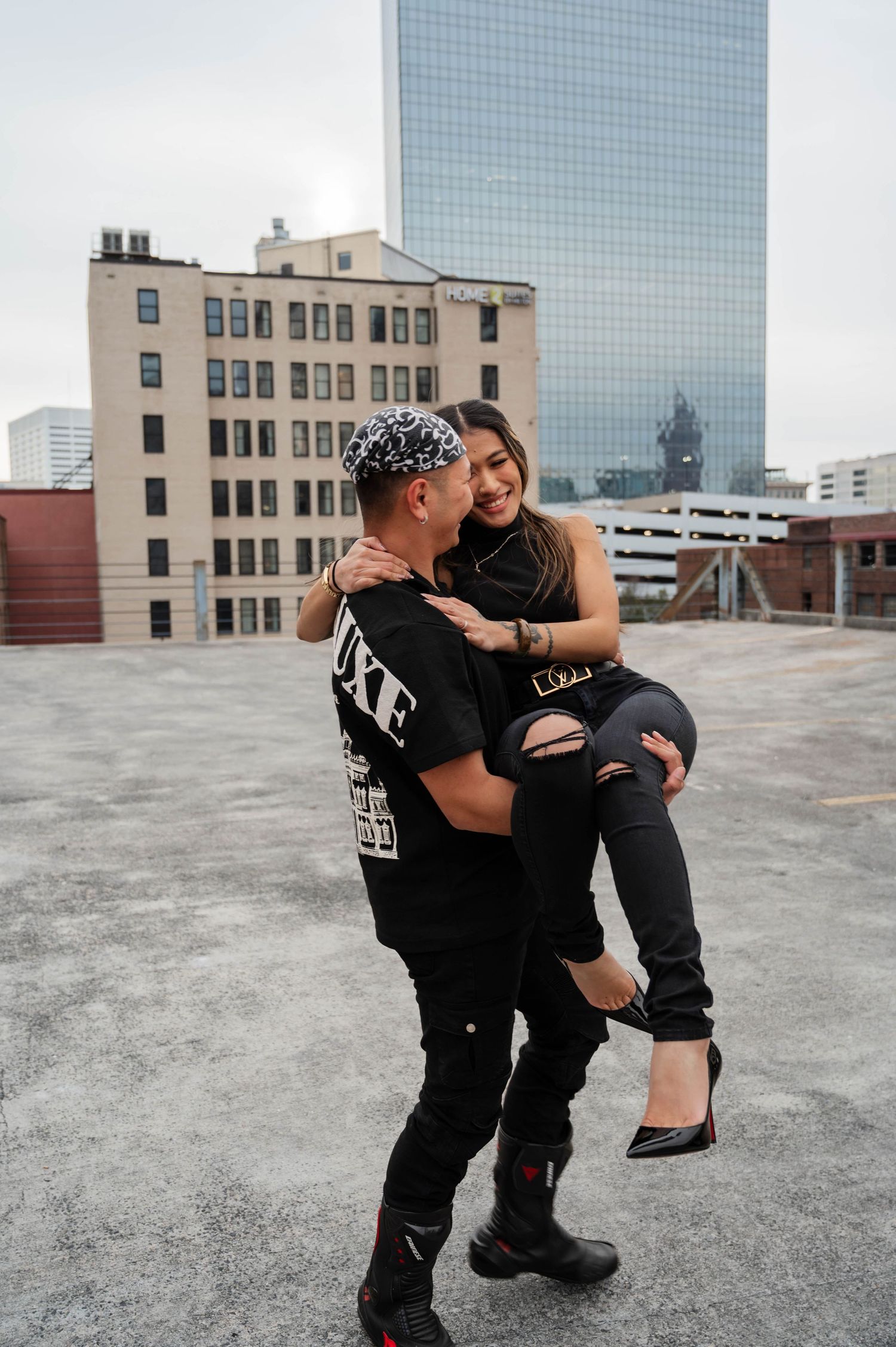 Two dancers in black outfits perform an urban dance routine on a rooftop with city buildings in the background.