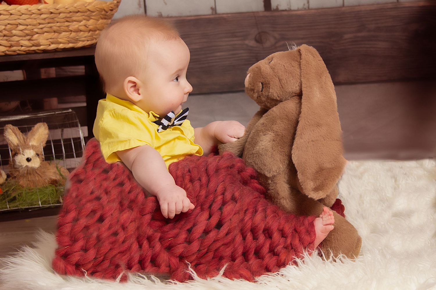 A small dog and baby interact while playing on a burgundy textured blanket on the floor.