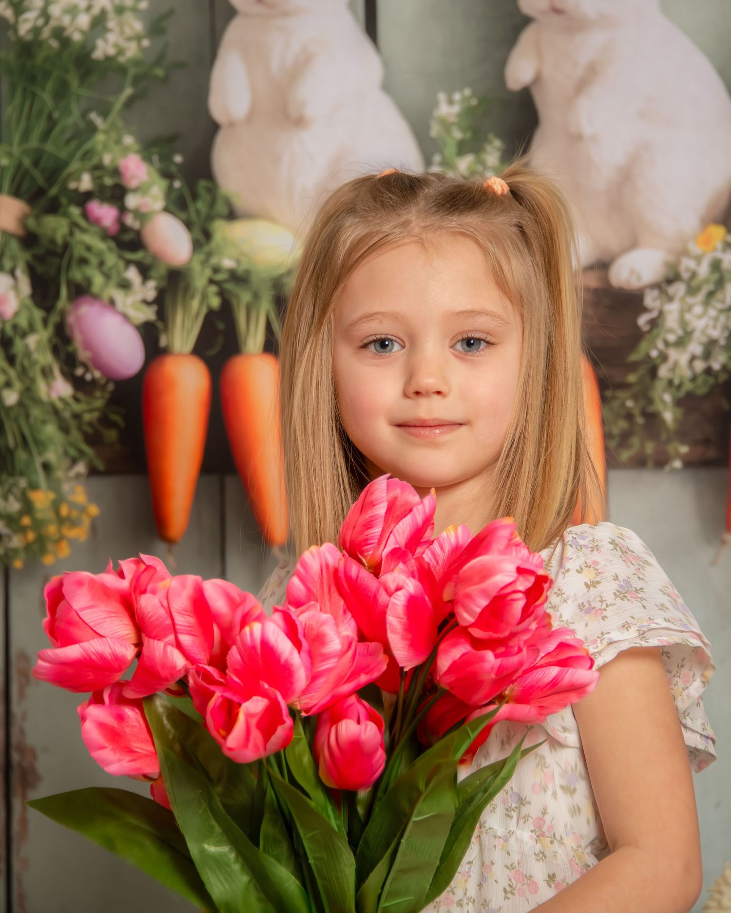 Easter spring photo session setup with pink tulips, decorative carrots, and soft bunny plush toys against a neutral backdrop.