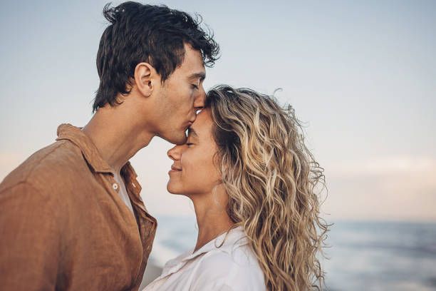 A romantic couple embraces against a soft sunset backdrop at the beach during a photoshoot.