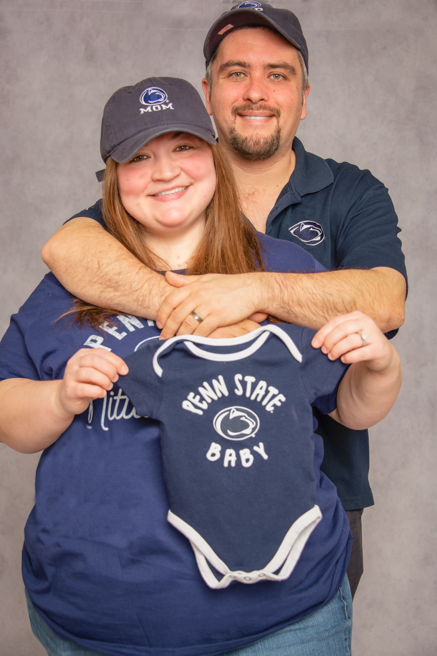 A couple holds up Penn State baby onesies in a series of four connected photos showing their excitement and joy.