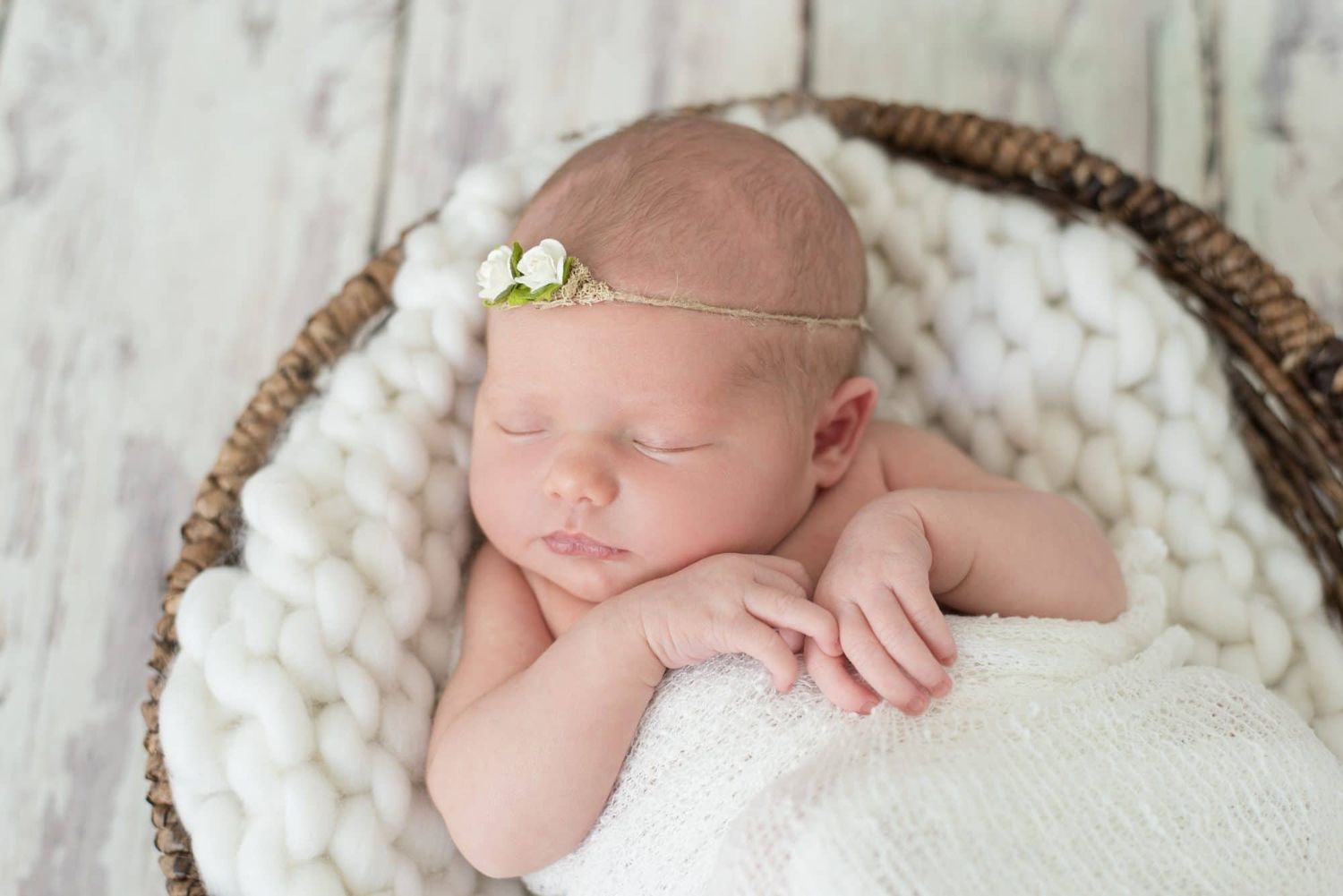 A sleeping newborn baby lies on soft white textured blankets in a peaceful pose during a professional photoshoot.