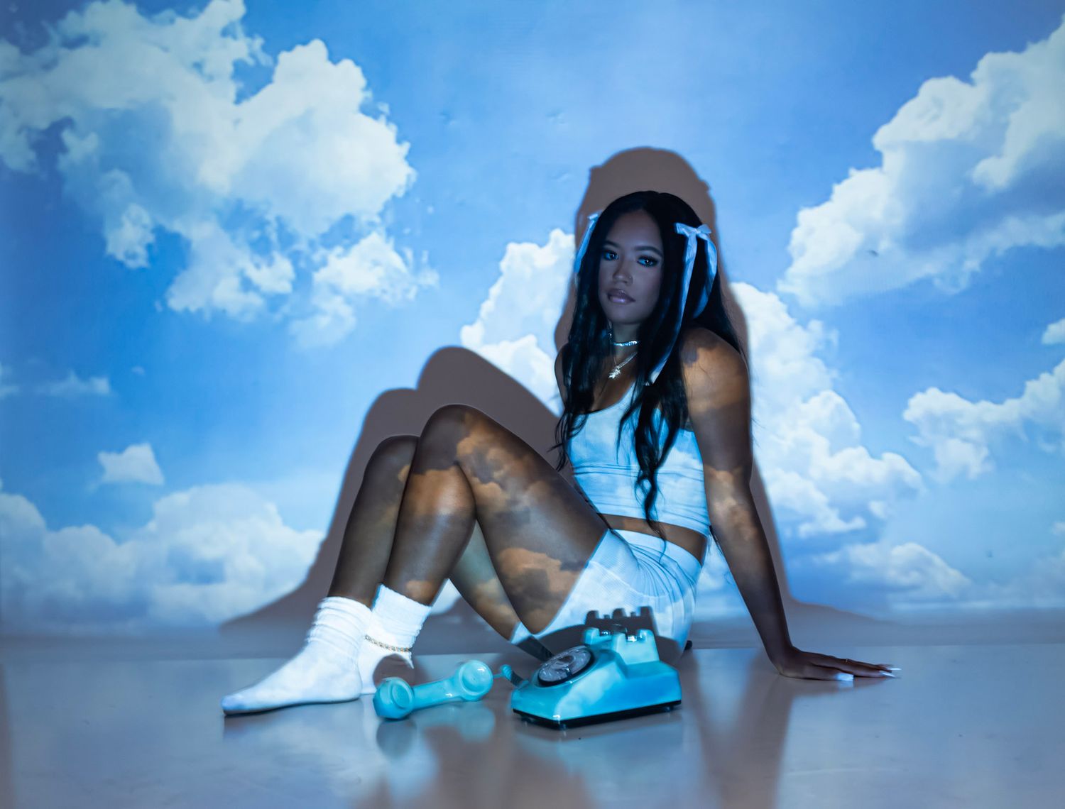 Dreamy beach-themed photoshoot against blue sky and clouds backdrop.