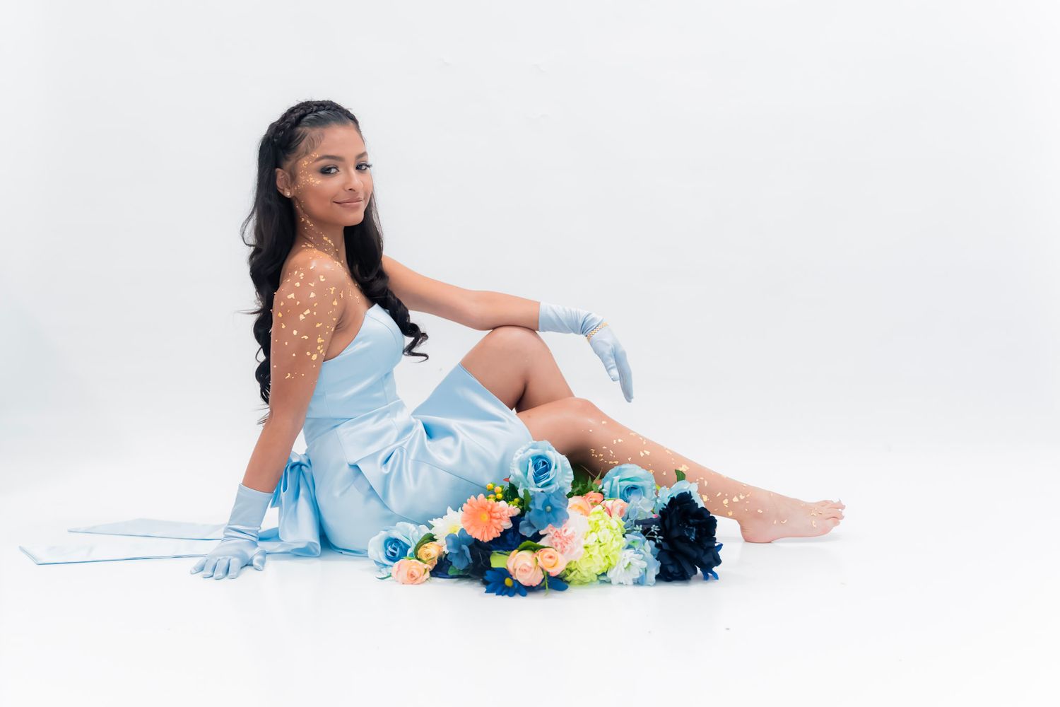 A dreamy portrait session with blue dress and colorful floral bouquet against white backdrop.