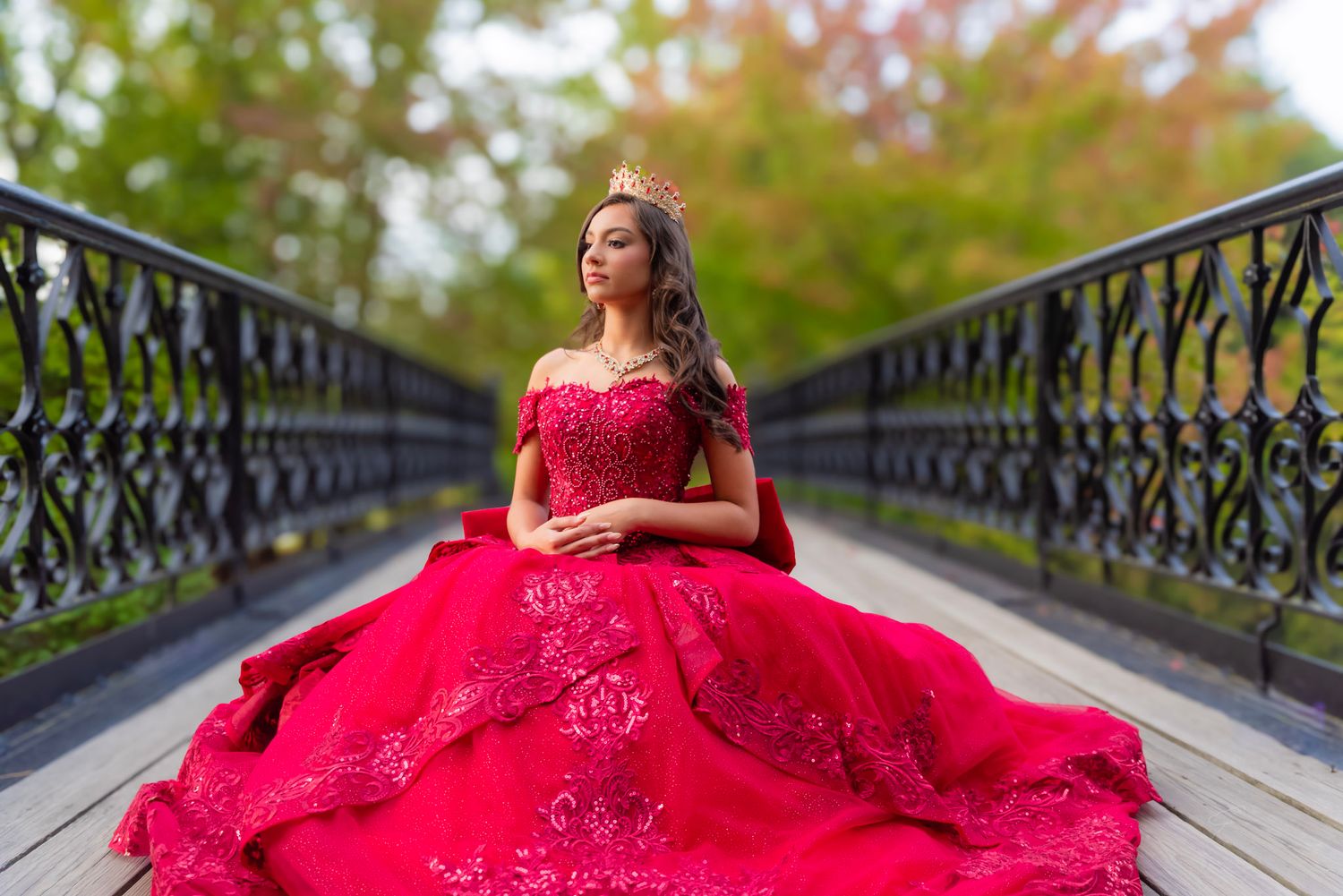 Dramatic red ball gown photo session on an ornate bridge with fall foliage.