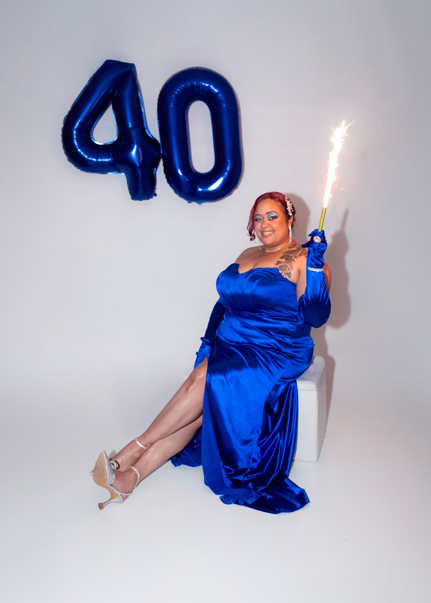 Woman in royal blue dress posing playfully with number 40 balloons against grey background.