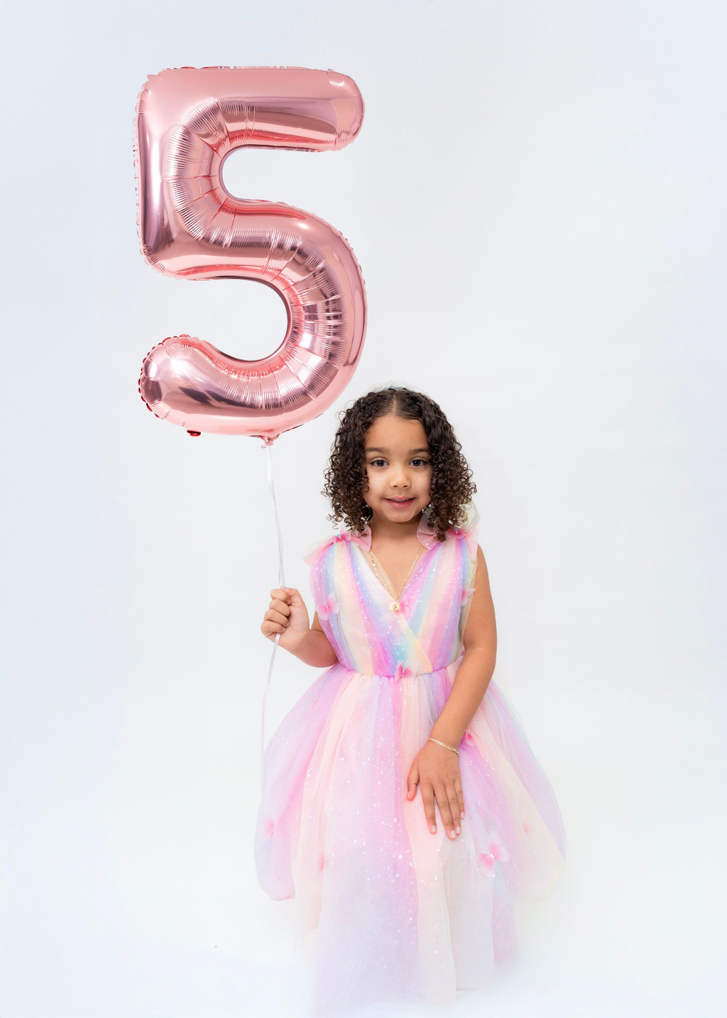 A birthday celebration with rose gold number 5 balloons and a pastel tulle dress against a white backdrop.