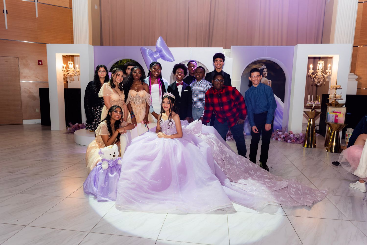 A group of people in formal attire dance and celebrate at an elegant wedding reception in a white-walled venue.