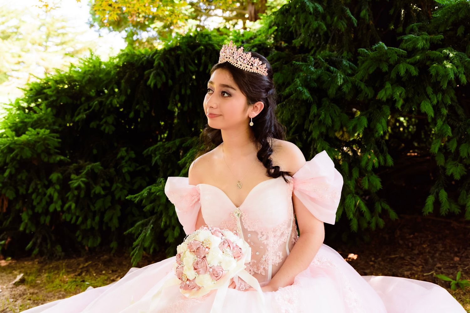 Outdoor Quinceañera portrait session featuring an elegant pink ballgown against natural greenery.