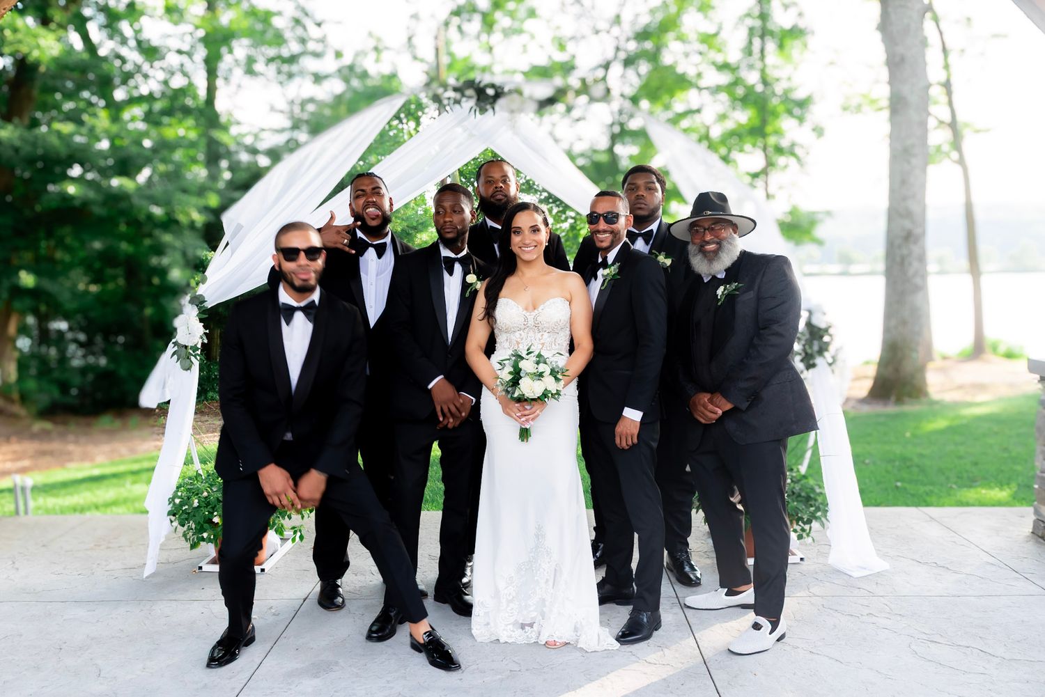Wedding party in formal attire walking and laughing together on a tree-lined path during an outdoor celebration.