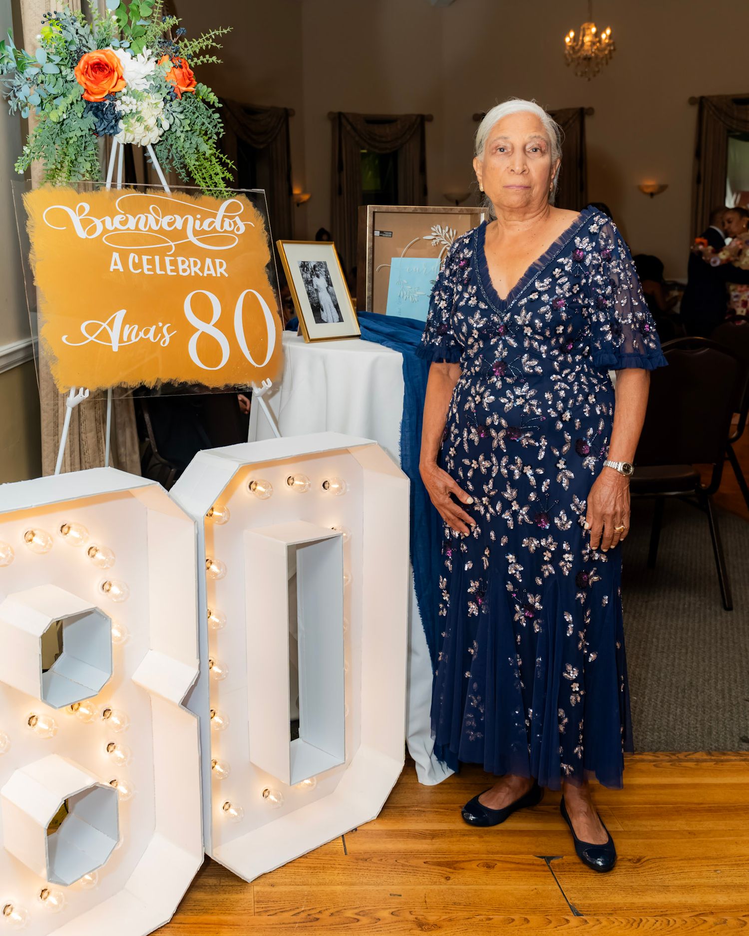 A celebratory scene with illuminated marquee letters and floral decorations for an 80th birthday party.