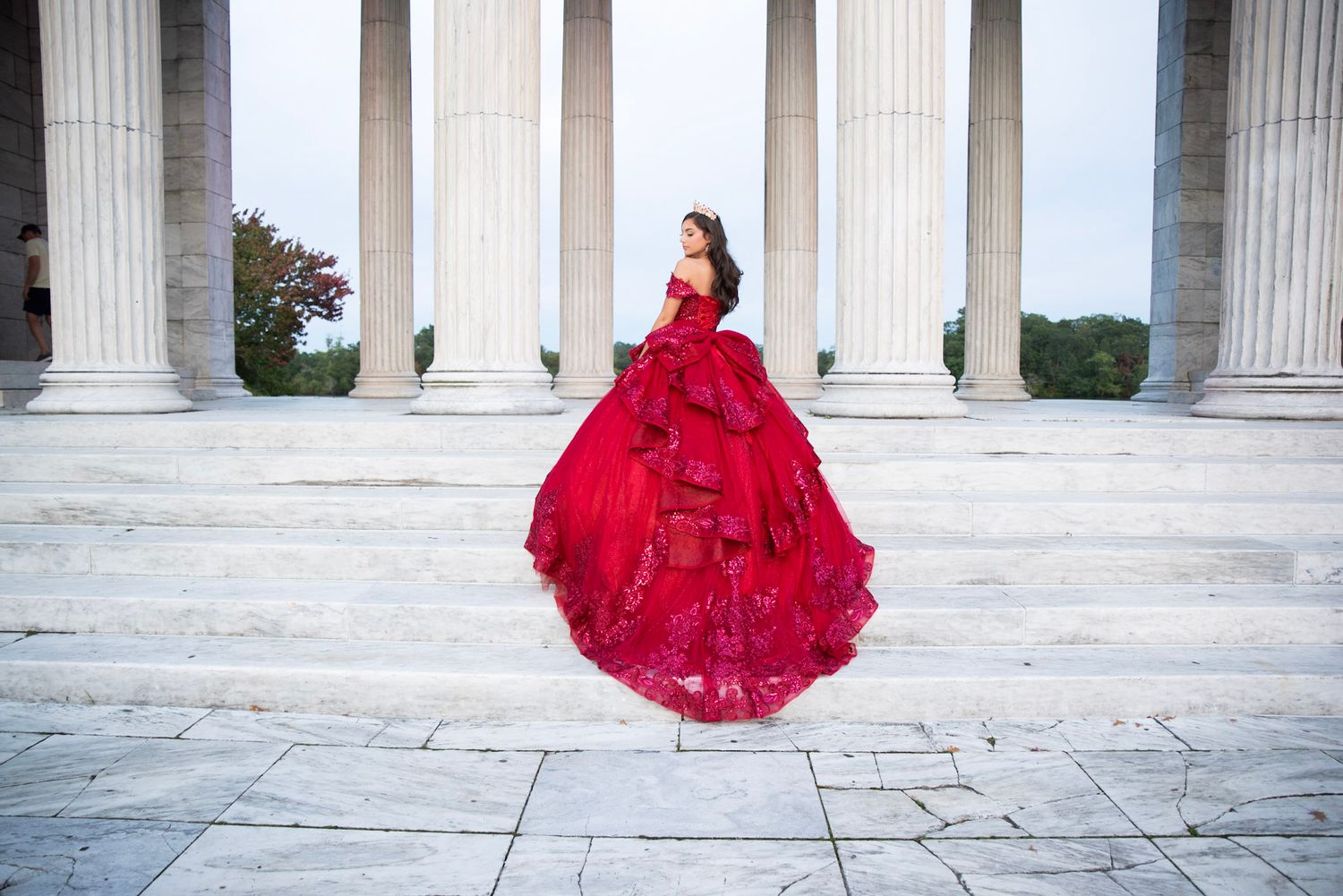 Sweeping red ball gown photos at a grand colonnade with white marble pillars.