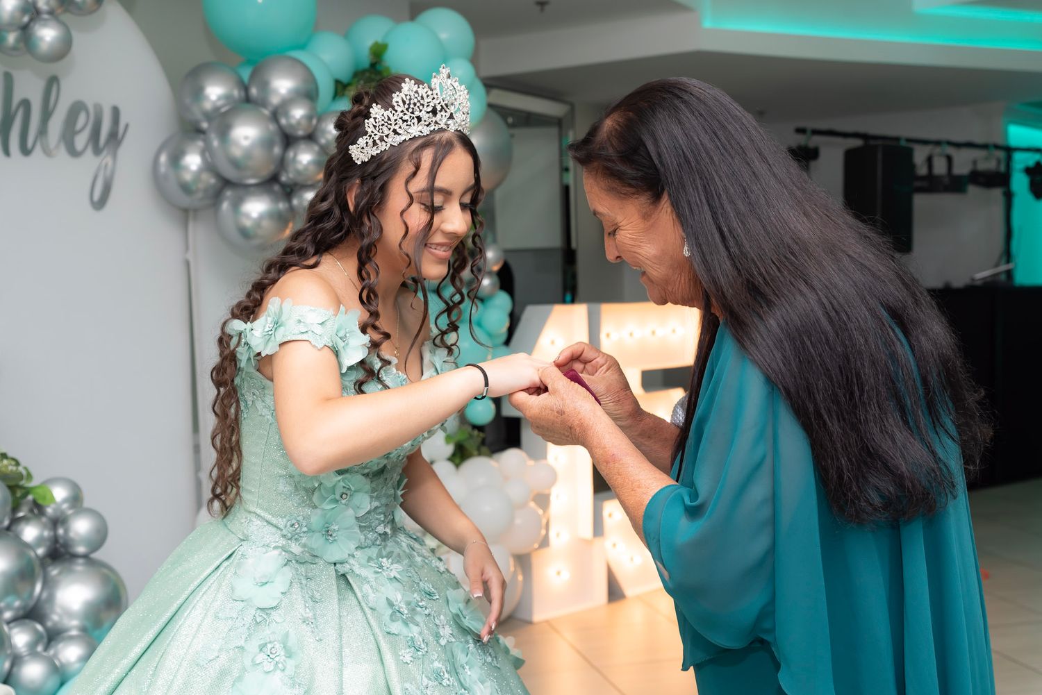 A celebratory moment at a quinceañera party decorated with mint green and silver balloon arches.