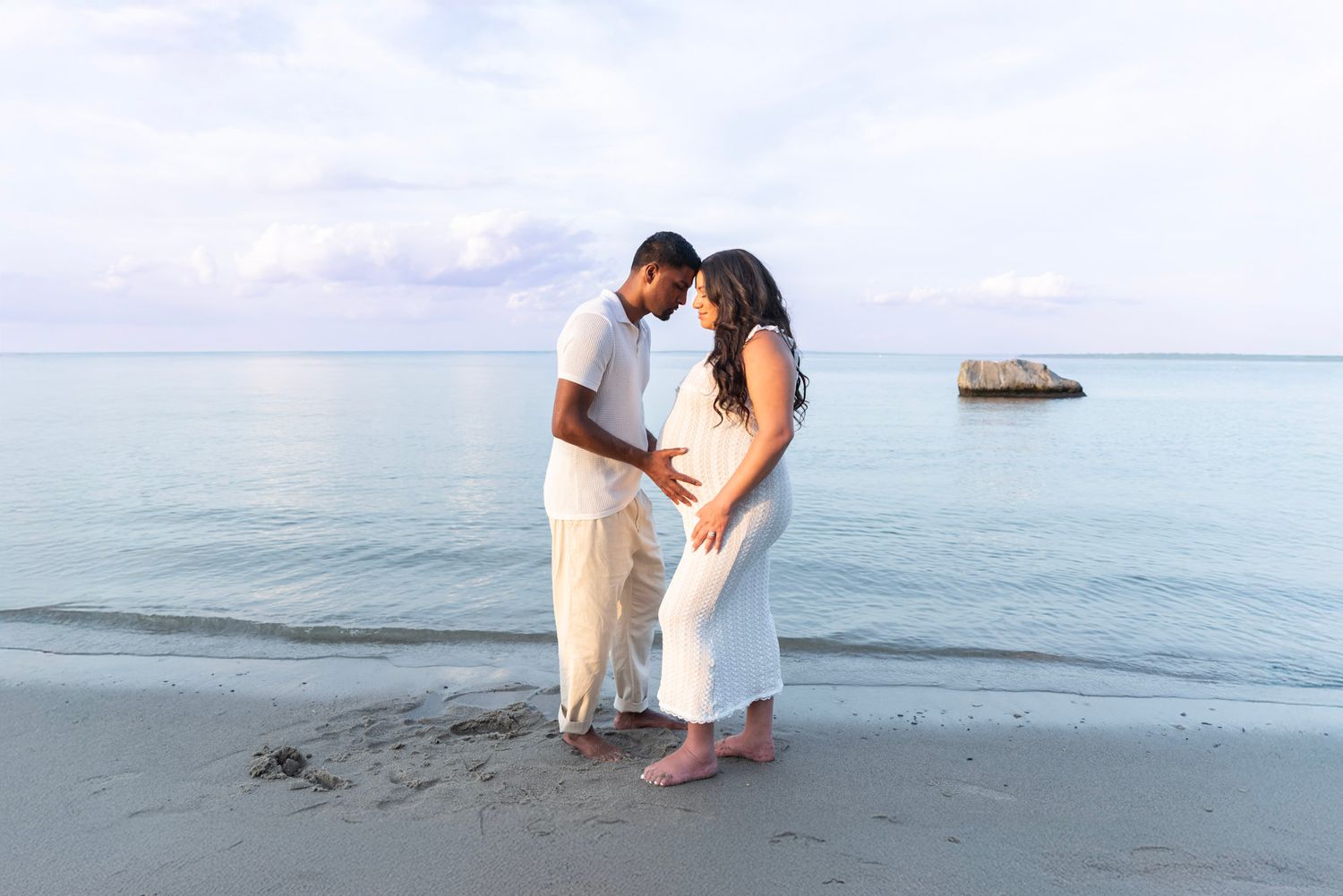 Casual beach engagement photos with waves and cloudy sky in background.