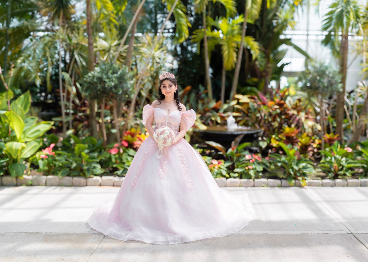 Elegant gown photographed in a lush tropical garden setting with palm trees and greenery.