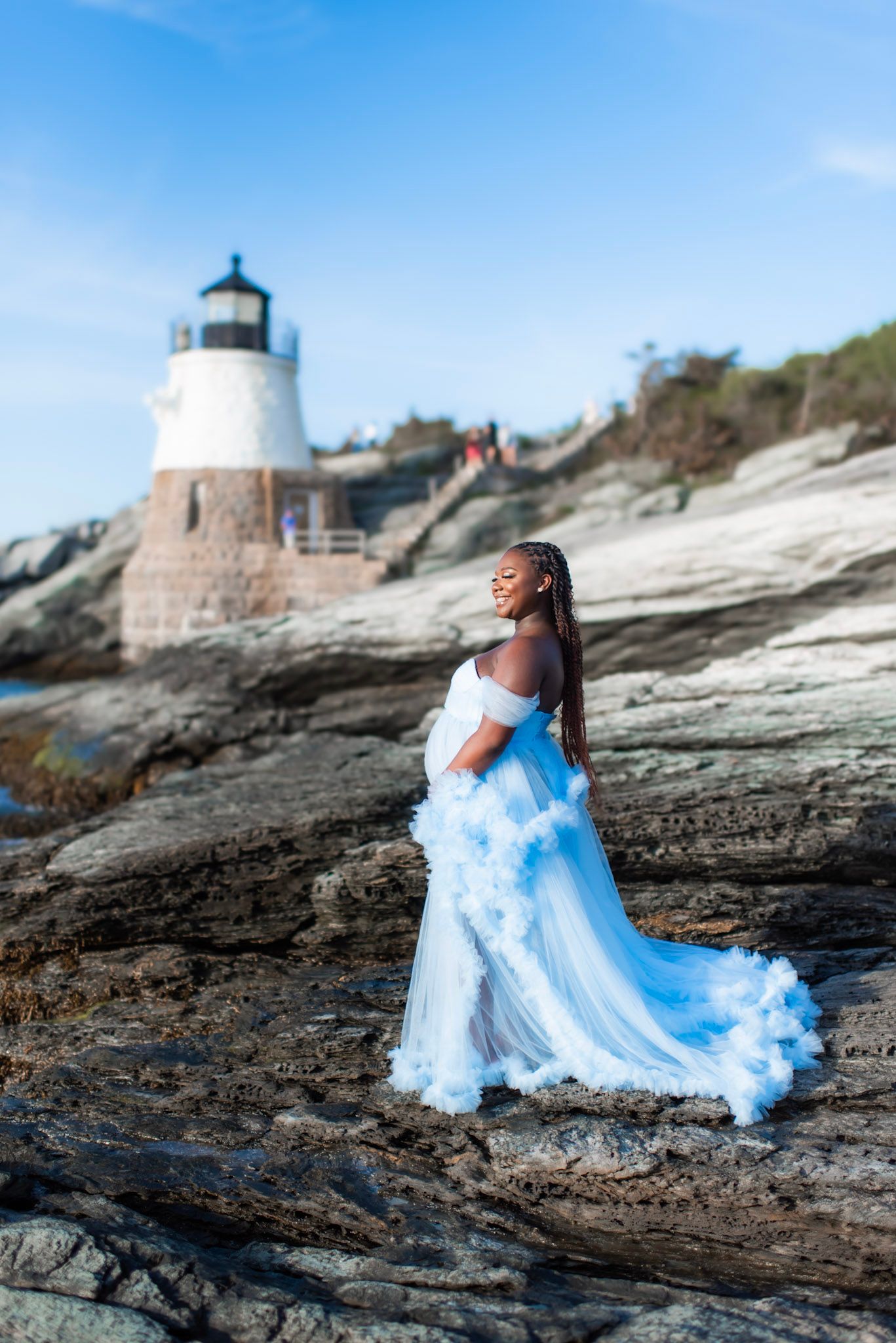 A flowing light blue dress photographed against rocky coastal terrain with a lighthouse in the background.