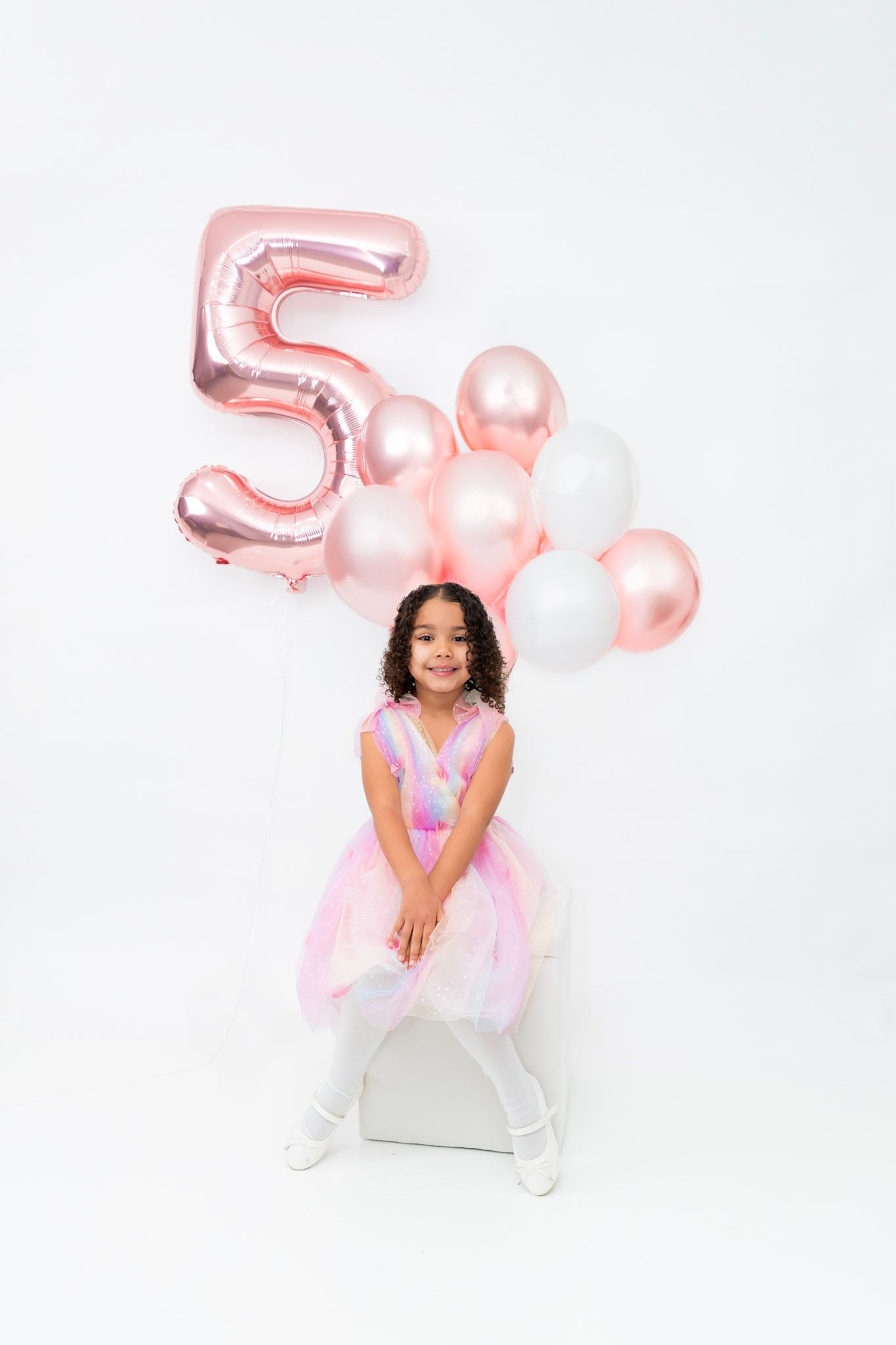 A festive photo shoot with pink number 5 balloons and white decorations in a studio setting.